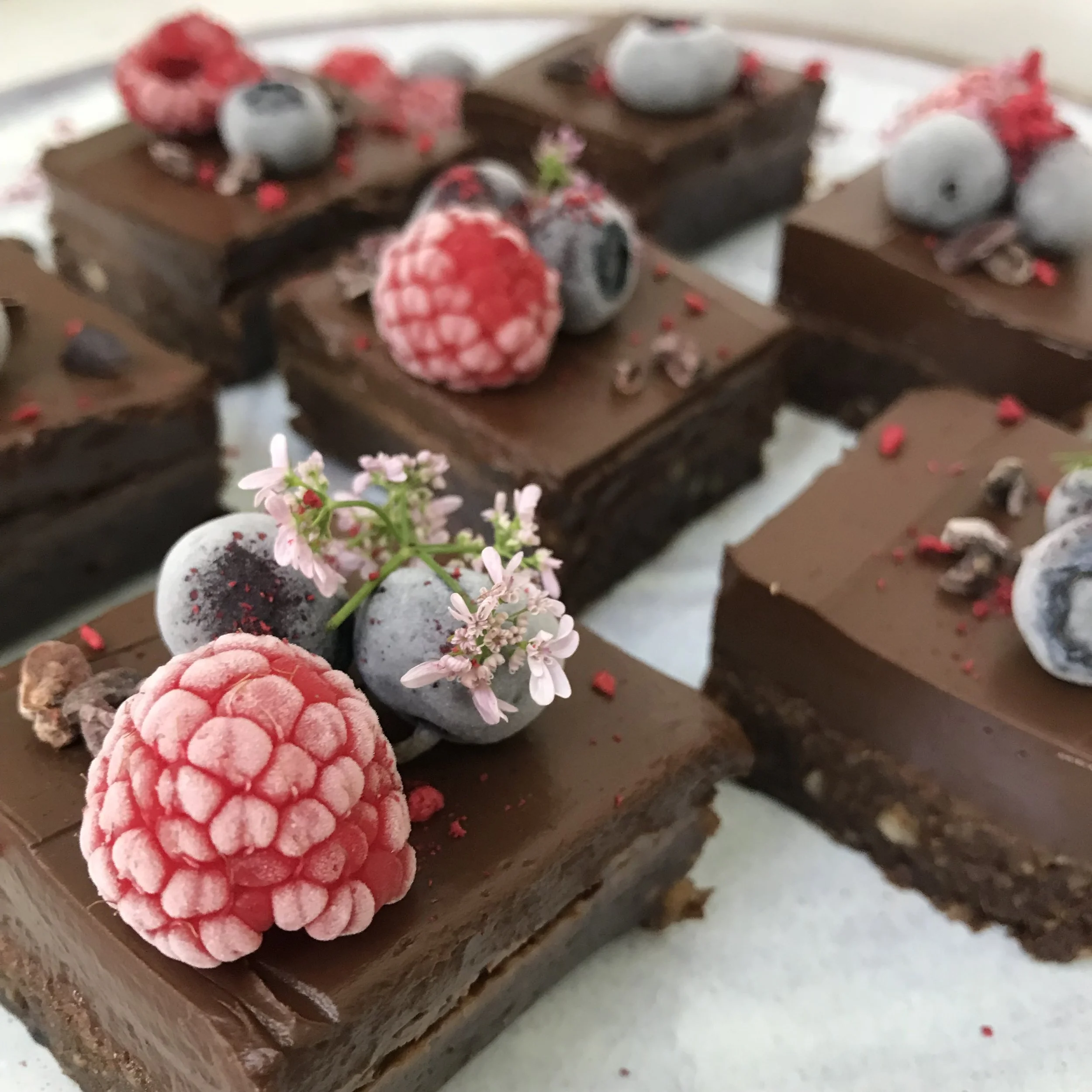 Close-up of chocolate brownie squares topped with fresh berries, edible flowers, and pink sprinkles.