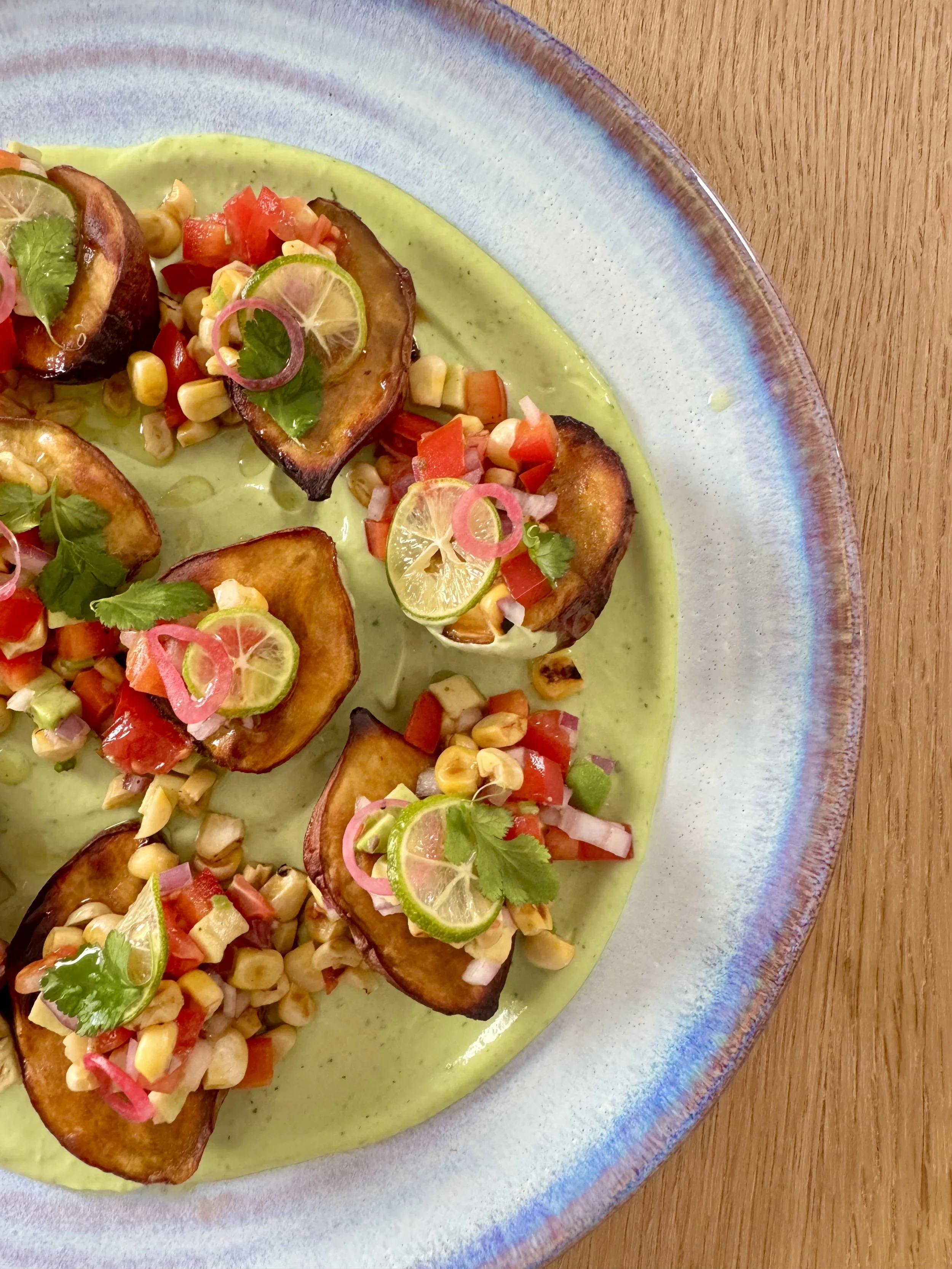 Close-up of a colorful dish with fried plantains topped with pico de gallo, lime slices, and cilantro, served on a ceramic plate.