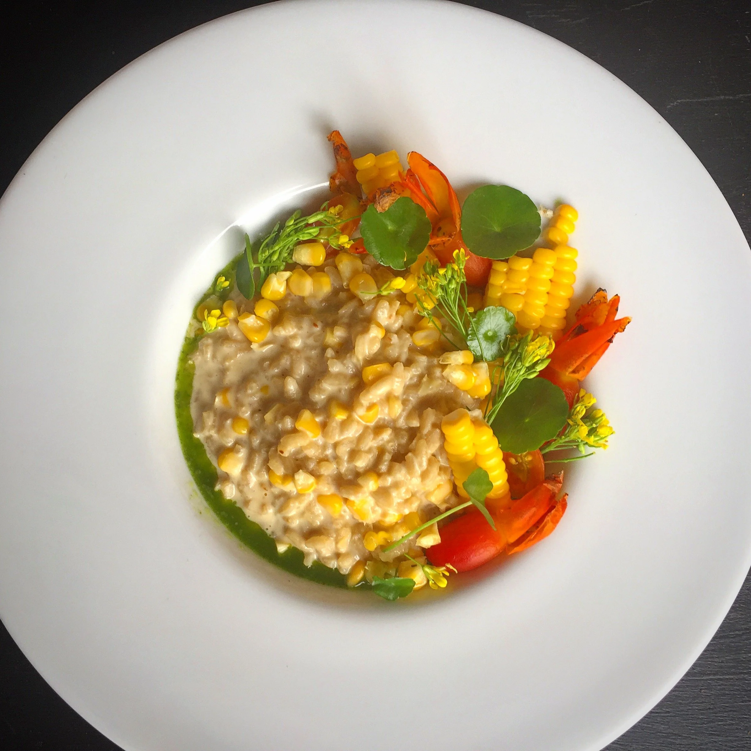Creamy risotto served with corn, cherry tomatoes, microgreens, and edible flowers on a white plate
