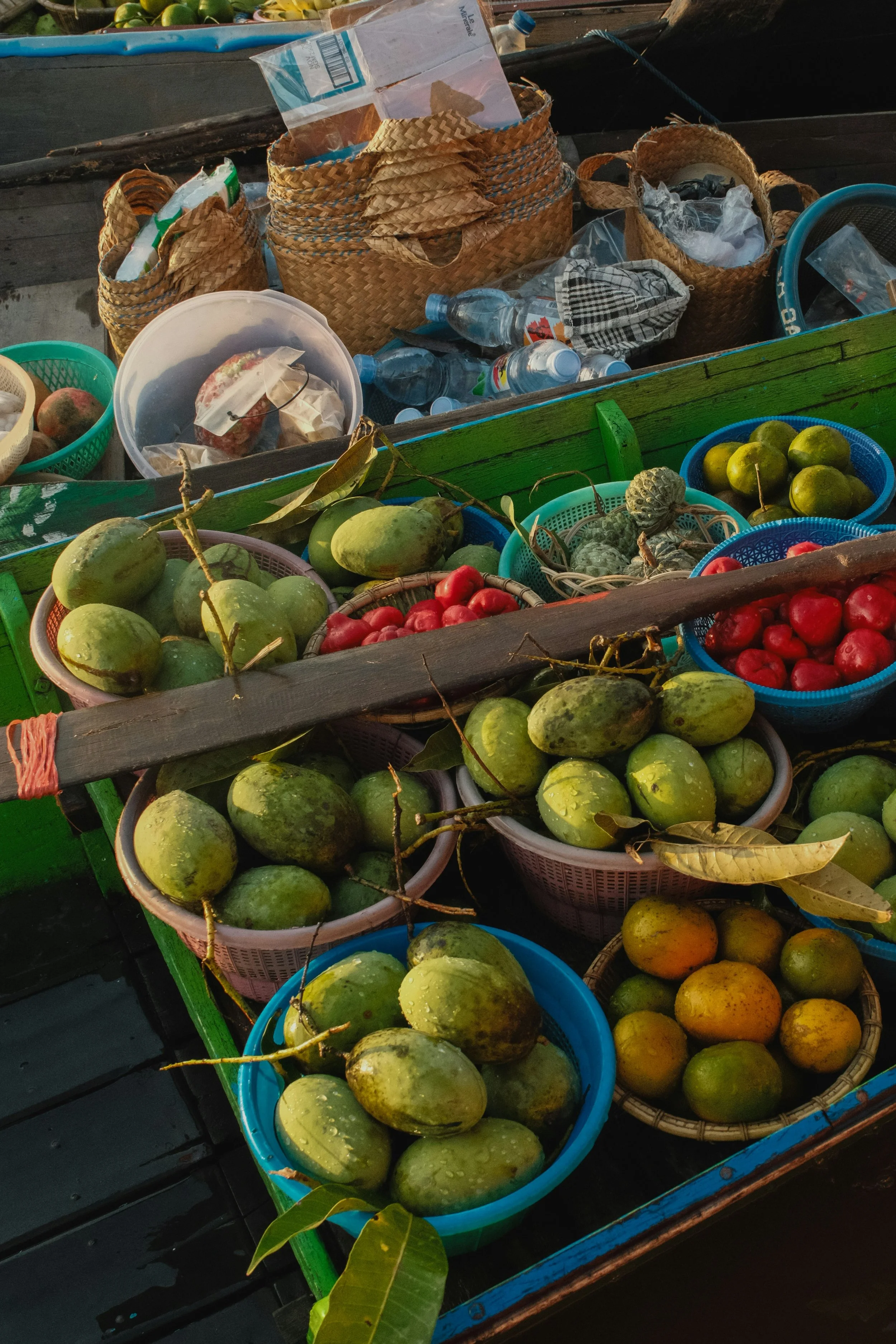 Panier et paniers remplis de fruits, notamment des mangues vertes, des tomates rouges, des limes vertes et des fruits jaunes, dans un marché à l'extérieur.