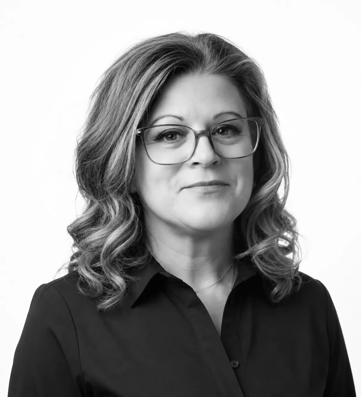 Black and white portrait of a woman with wavy hair, wearing glasses and a dark shirt, looking confidently at the camera.