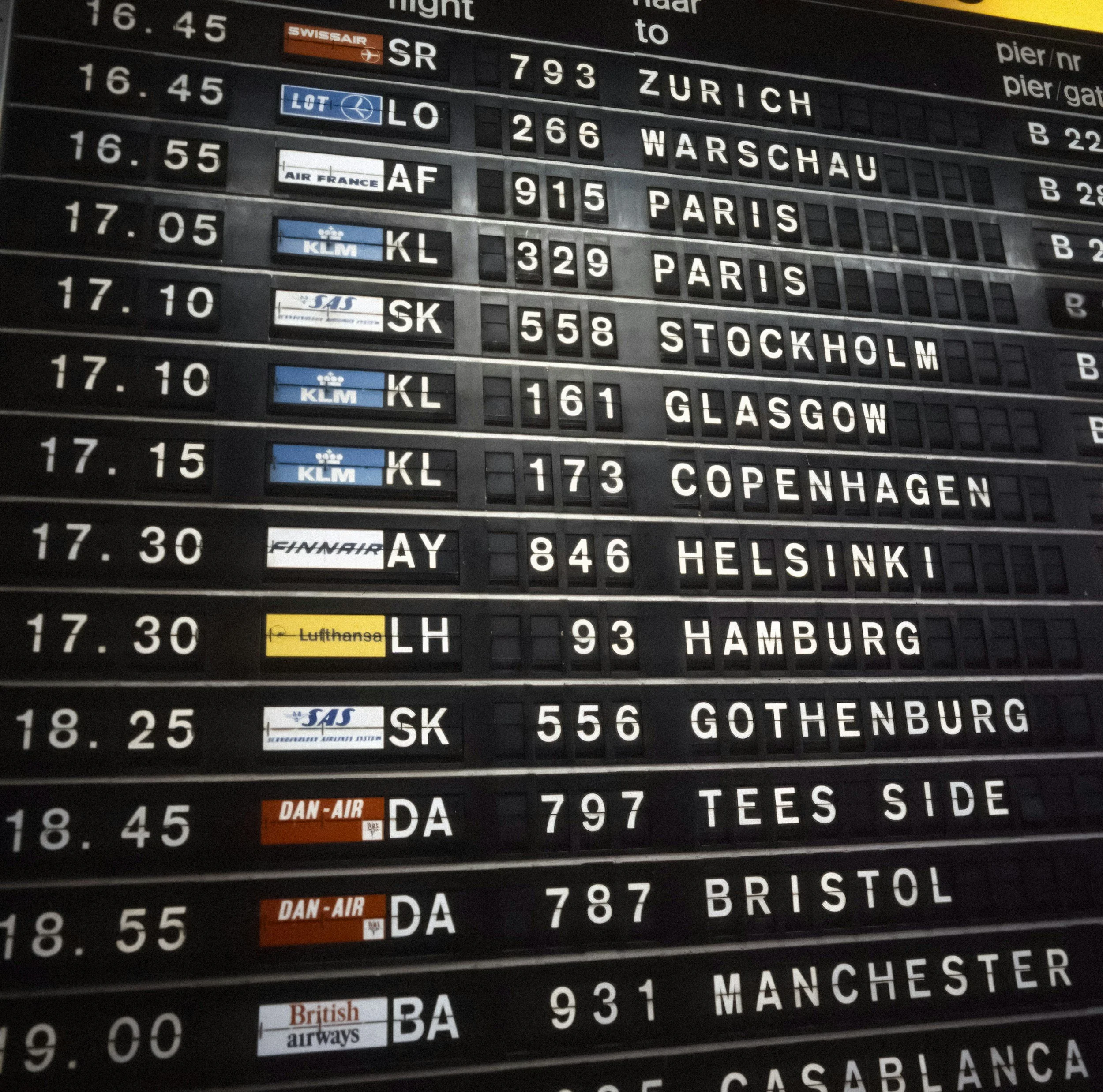 Airport departure information display board showing flight details to Zurich, Warsaw, Paris, Stockholm, Copenhagen, Hamburg, and others with scheduled times and airline logos.