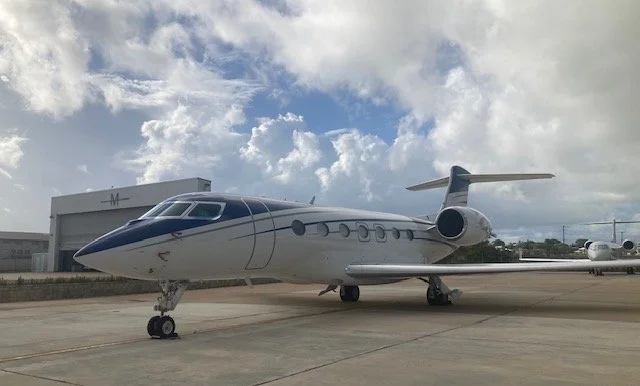 A private jet parked on an airport tarmac with a cloudy sky in the background.