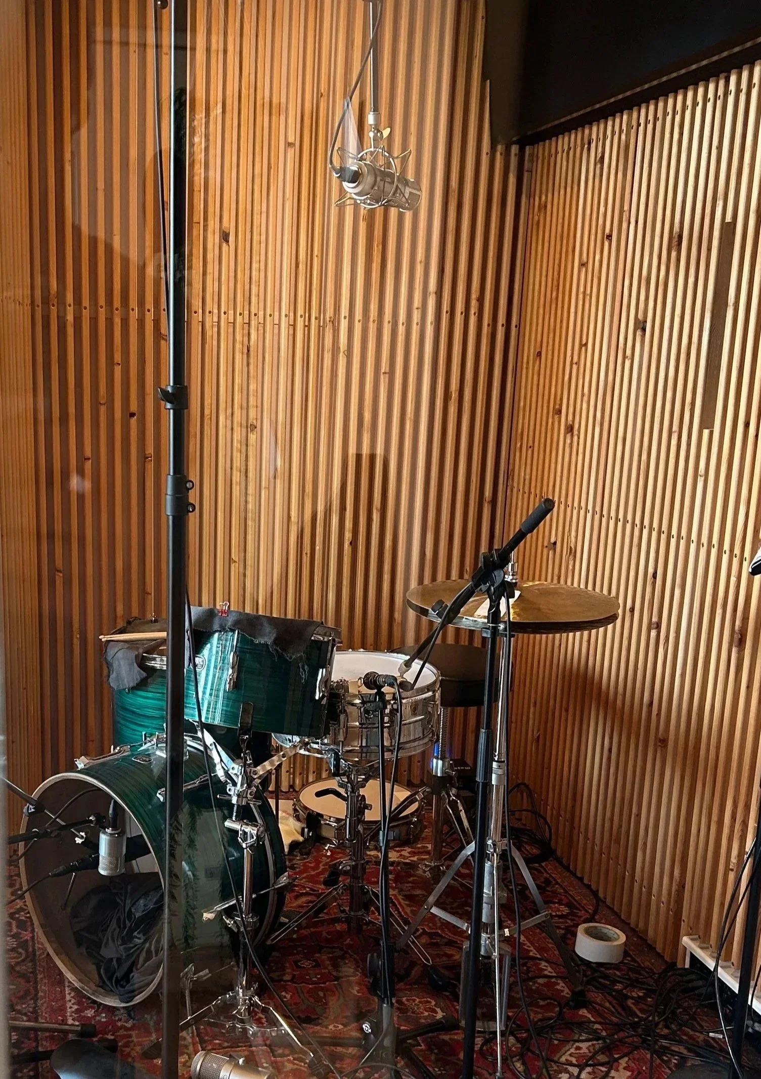 A green, single headed 1960's Premier Olympic drumkit with Ludwig Supraphonic snare drum in a small drum booth with wooden panels. Warm light. Several microphones around the drums.