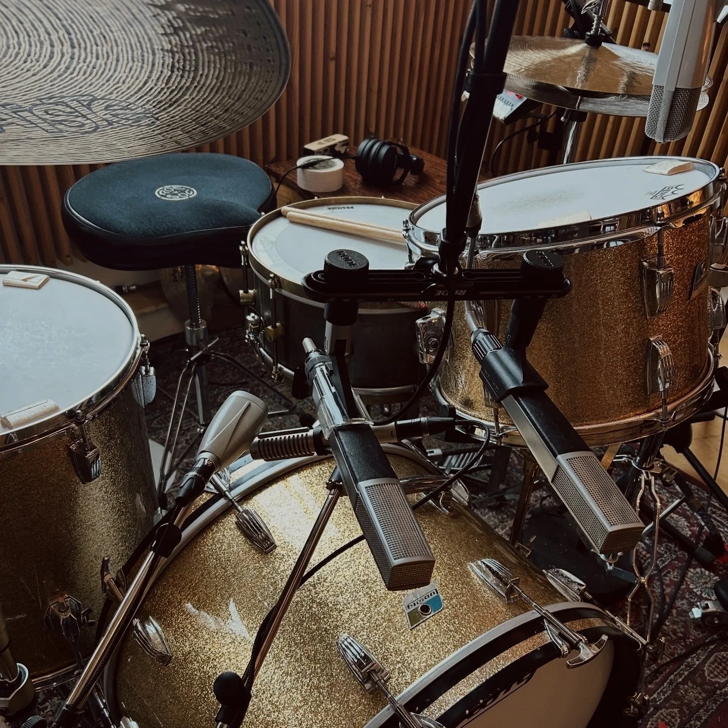 Close up of a 1970's Ludwig drum kit in champagne sparkle with a A&F Raw Brass Snare and Paiste cymbals in a recording studio. The drums are fully mic'ed with Sennheiser MD441 and MD421 microphones. The Studio has wooden panels on the walls.