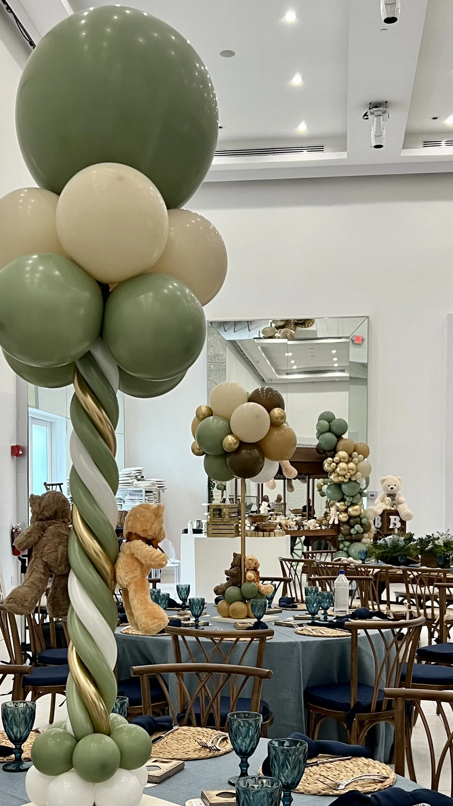 Decorated party room with large balloon bouquets, teddy bears, and table settings. Balloon and teddy bear centerpieces, cart rental decor