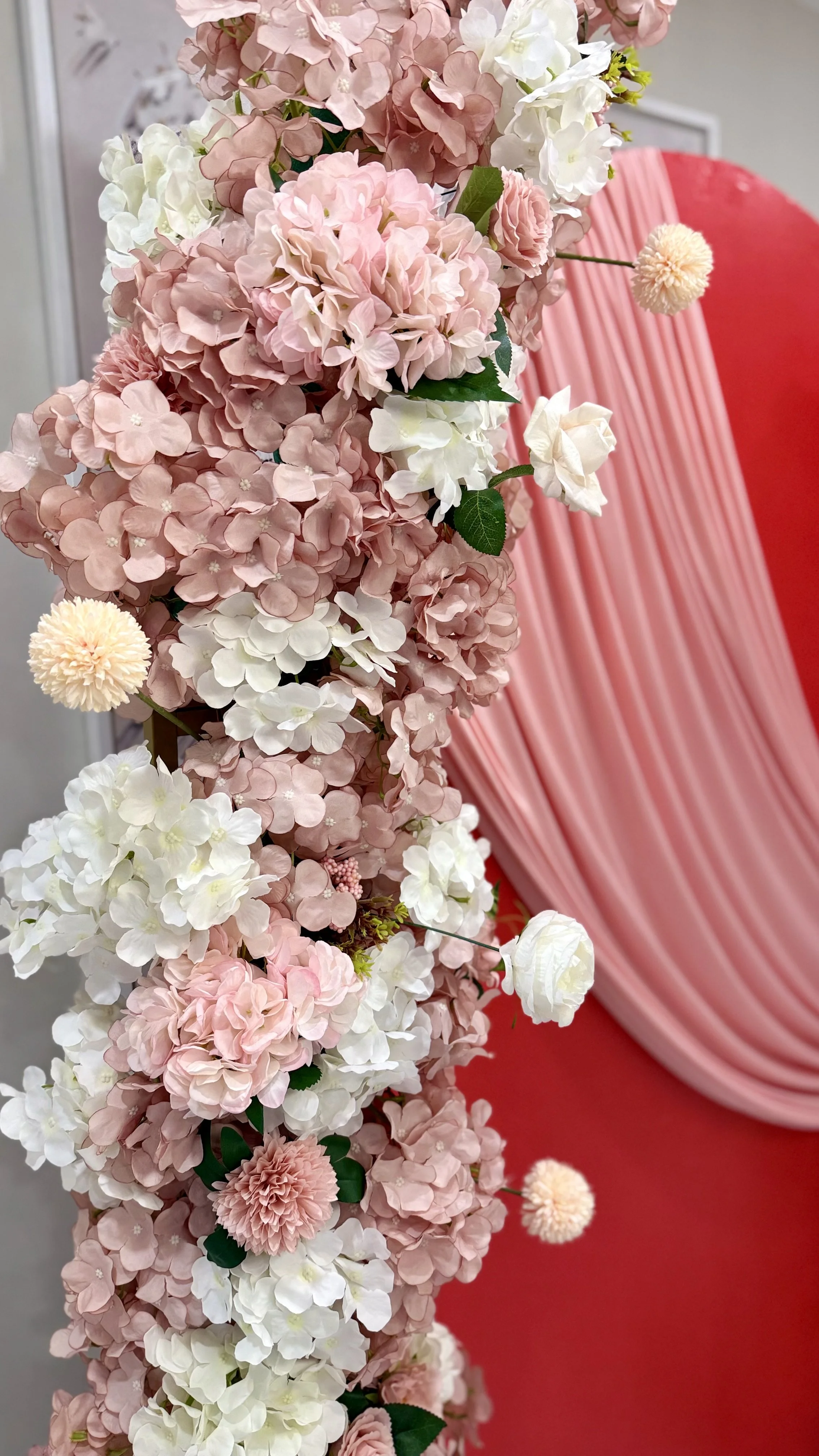 Close-up of a floral arrangement with pink, white, and peach hydrangeas and chrysanthemums in front of a pink draped backdrop.