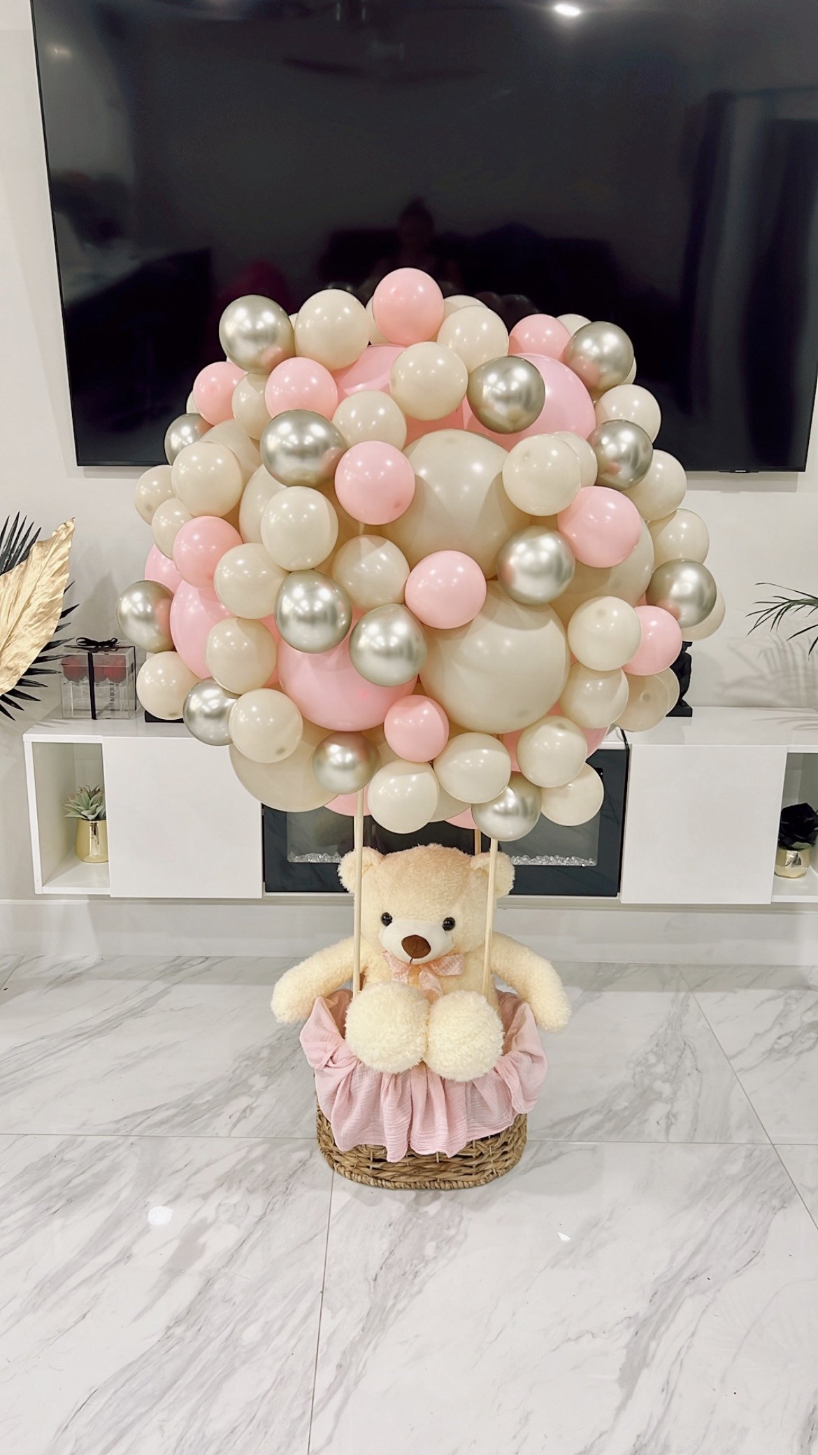 Decorative teddy bear with balloons in pink, white, and silver, in a wicker basket with pink fabric. Teddy Bear in Hot Air Balloon Basket