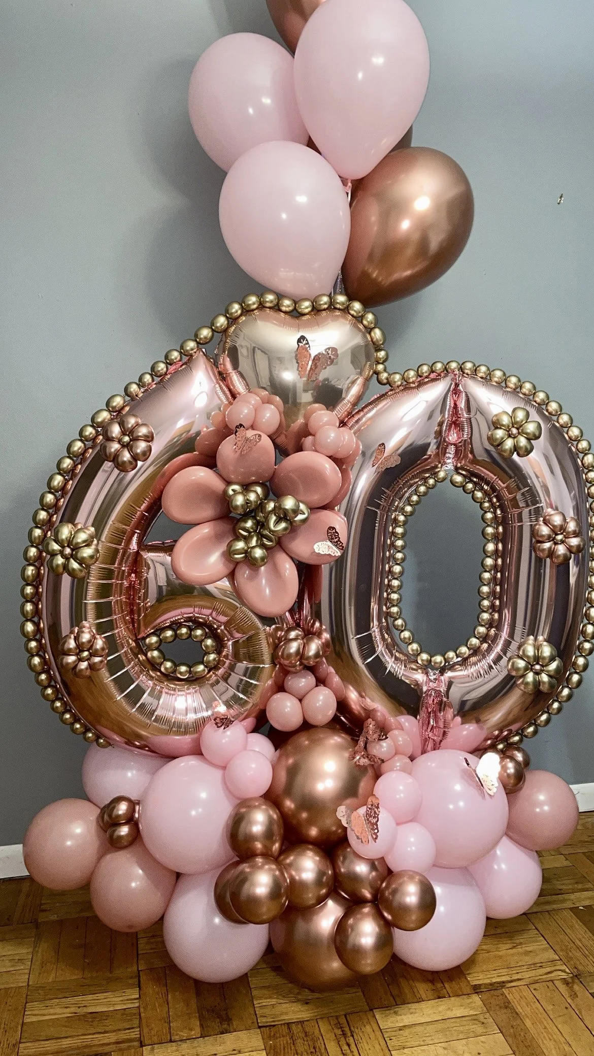 Decorative balloon arrangement featuring pink and metallic gold balloons, including two large foil number balloons '4' and '0', with smaller balloons, butterfly stickers, and floral embellishments.