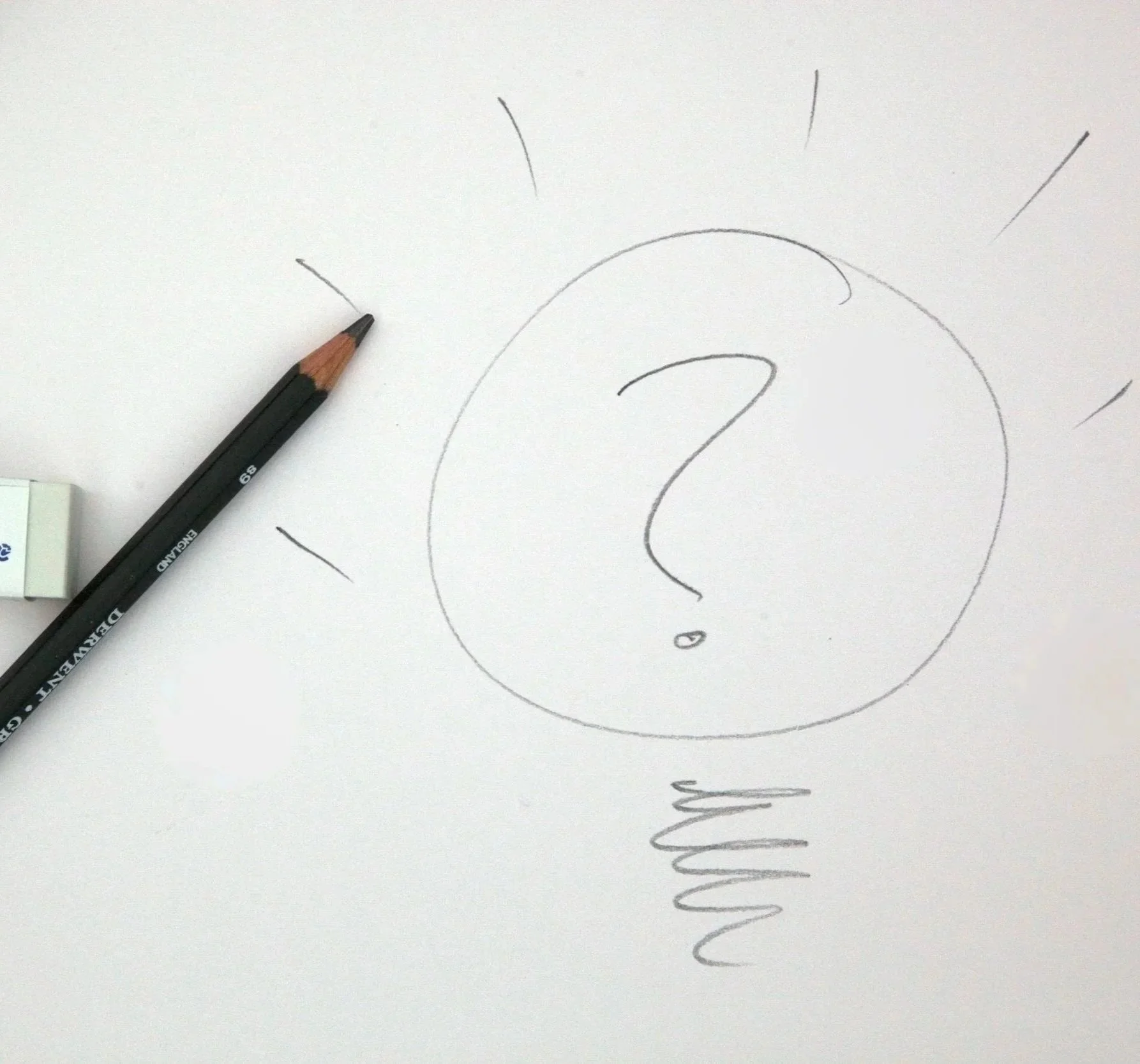 A white sheet of paper with a hand-drawn light bulb, a question mark inside the bulb, and lines radiating outward. A black pencil rests on the left side of the paper.