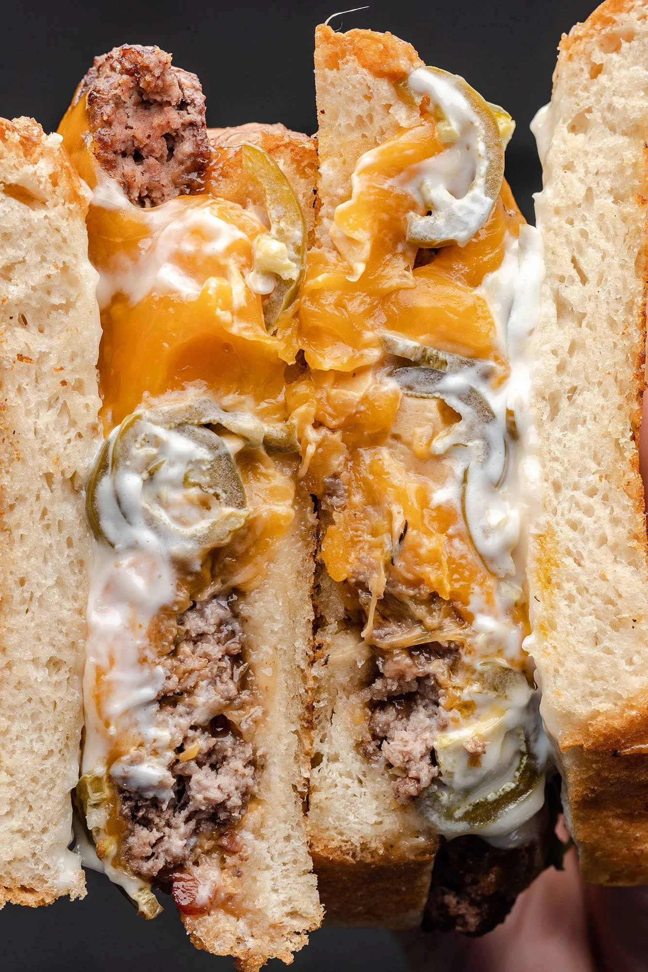 Close-up of a large, cut sandwich with bread, melted cheese, pickles, mayonnaise, and ground beef inside.