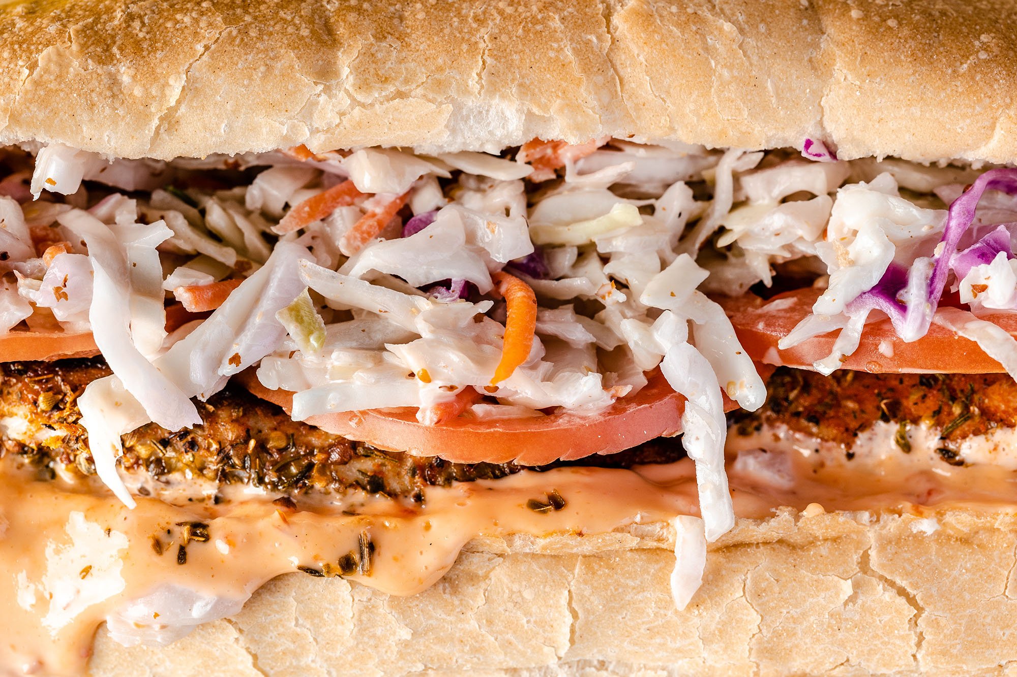 Close-up of a submarine sandwich with coleslaw, tomato, and sauce in a bread bun.