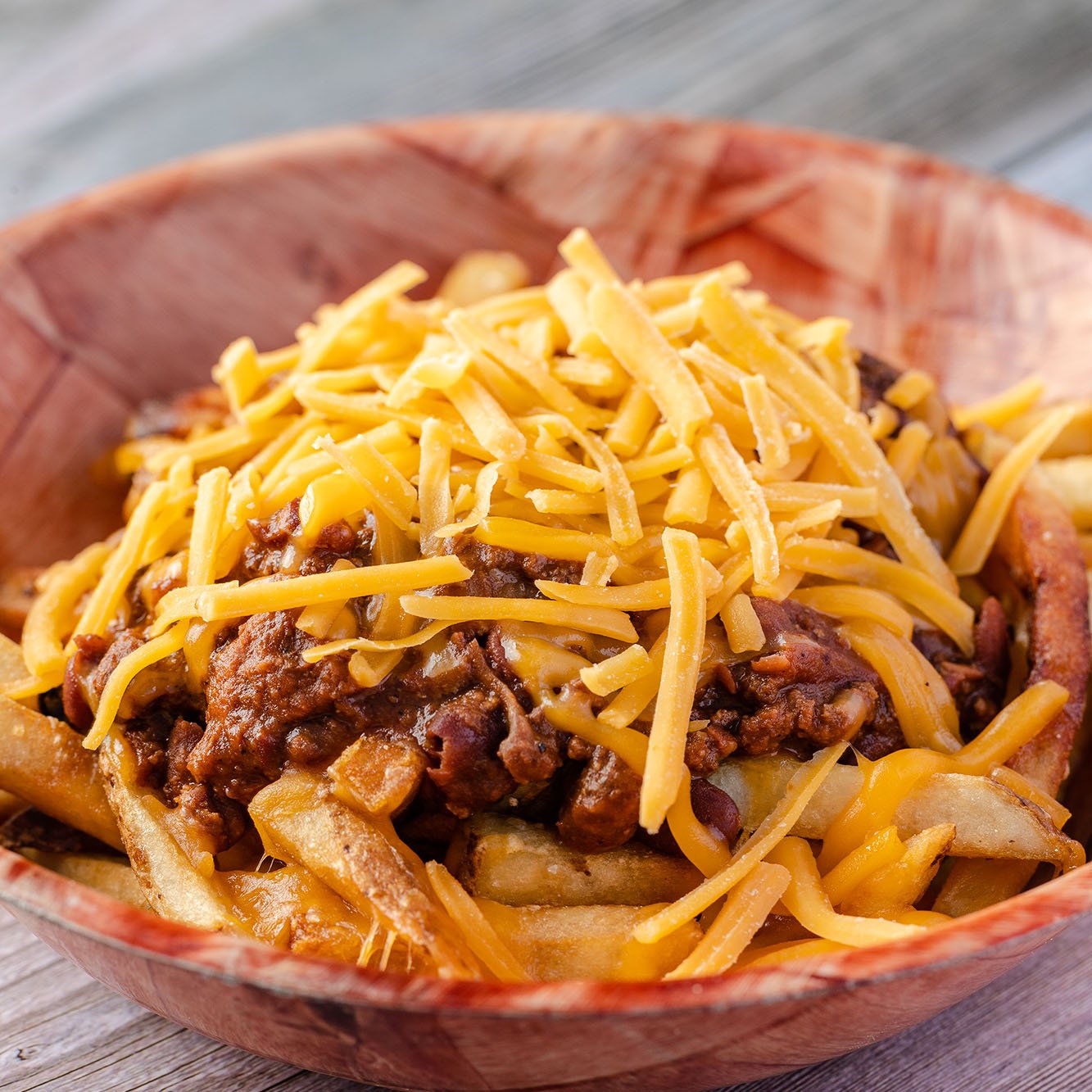 Close-up of a bowl with beef, cheese, and fries topped with shredded cheese.