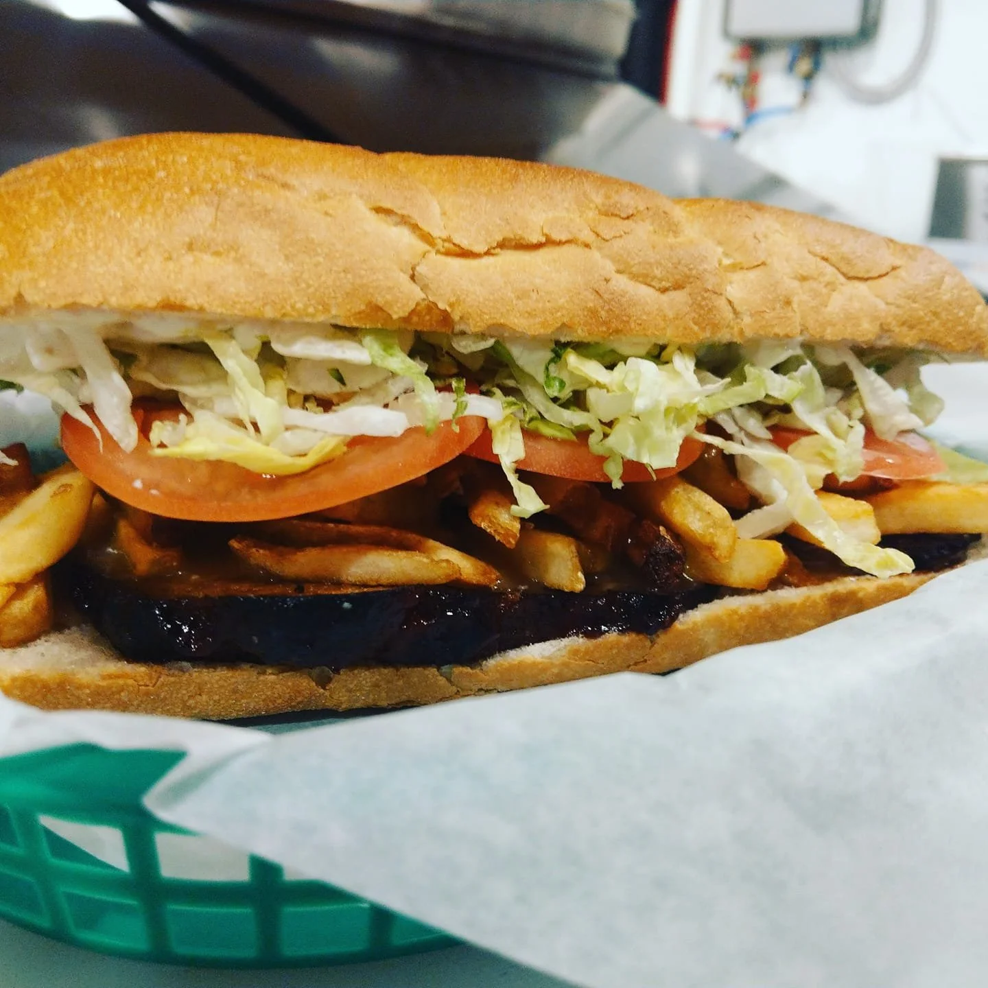 A submarine sandwich with lettuce, tomato, grilled vegetables, and toasted bread, served in a green basket lined with white paper.