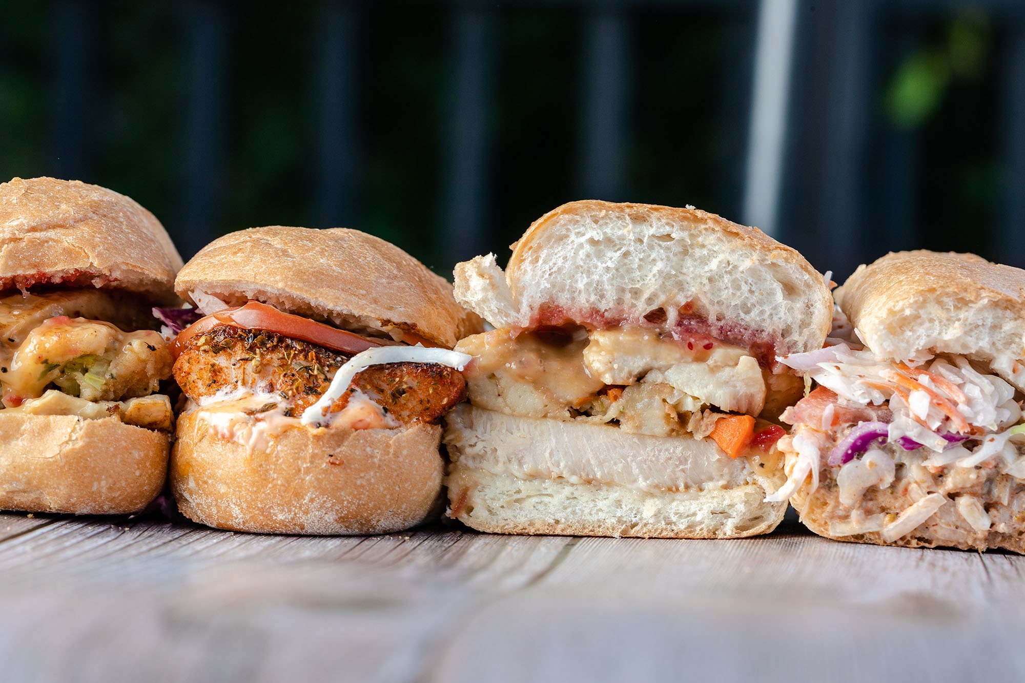 Close-up of four sandwiches on a wooden surface, with a blurred background.
