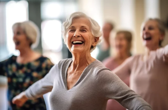 An elderly woman in a gray shirt exercising with a group of women in the background
