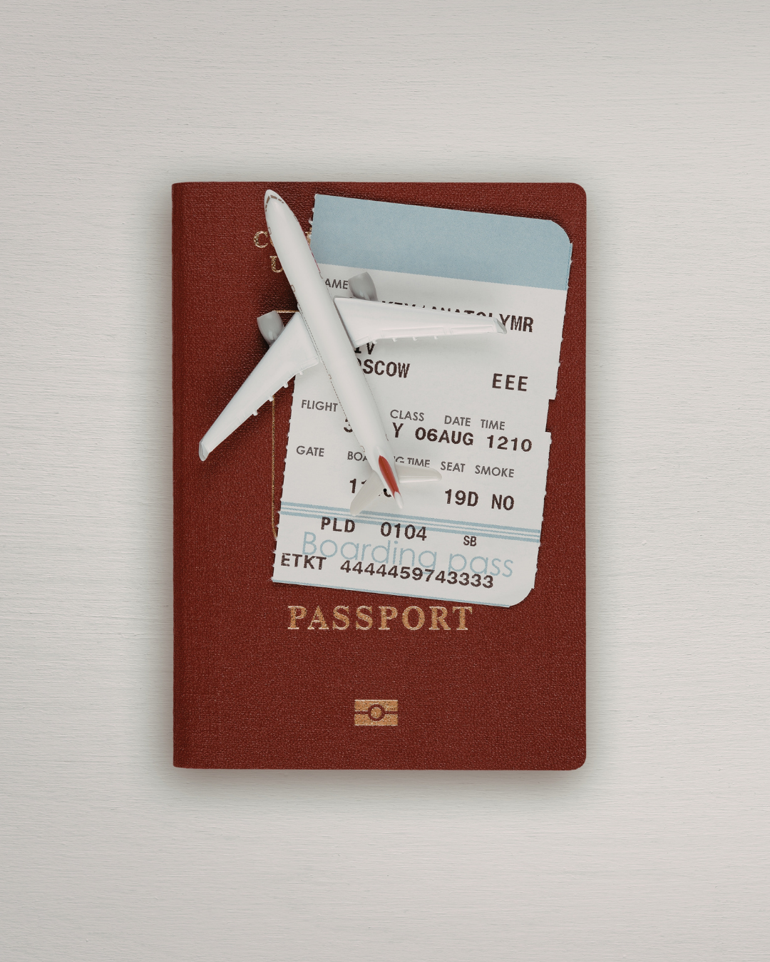 red, closed passport book with half of flight ticket and small model airplane resting neatly on top of passport book