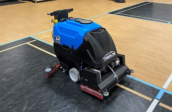 A ride-on floor buffer or scrubbing machine operating on a gymnasium or basketball court.
