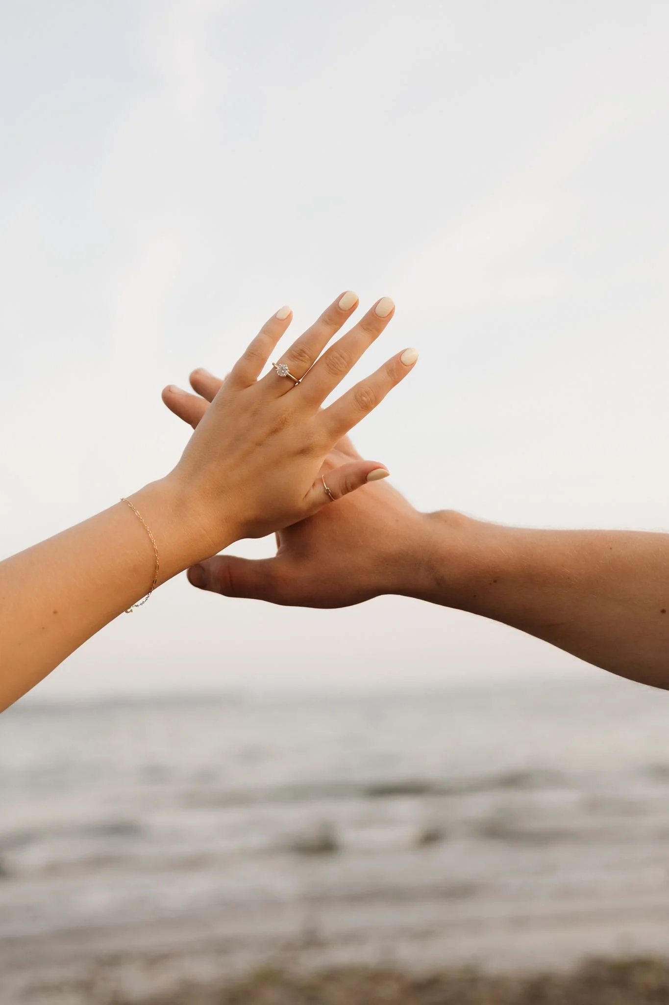 Two hands reaching towards each other with one hand wearing a ring and the other hand slightly below, against a cloudy sky background.