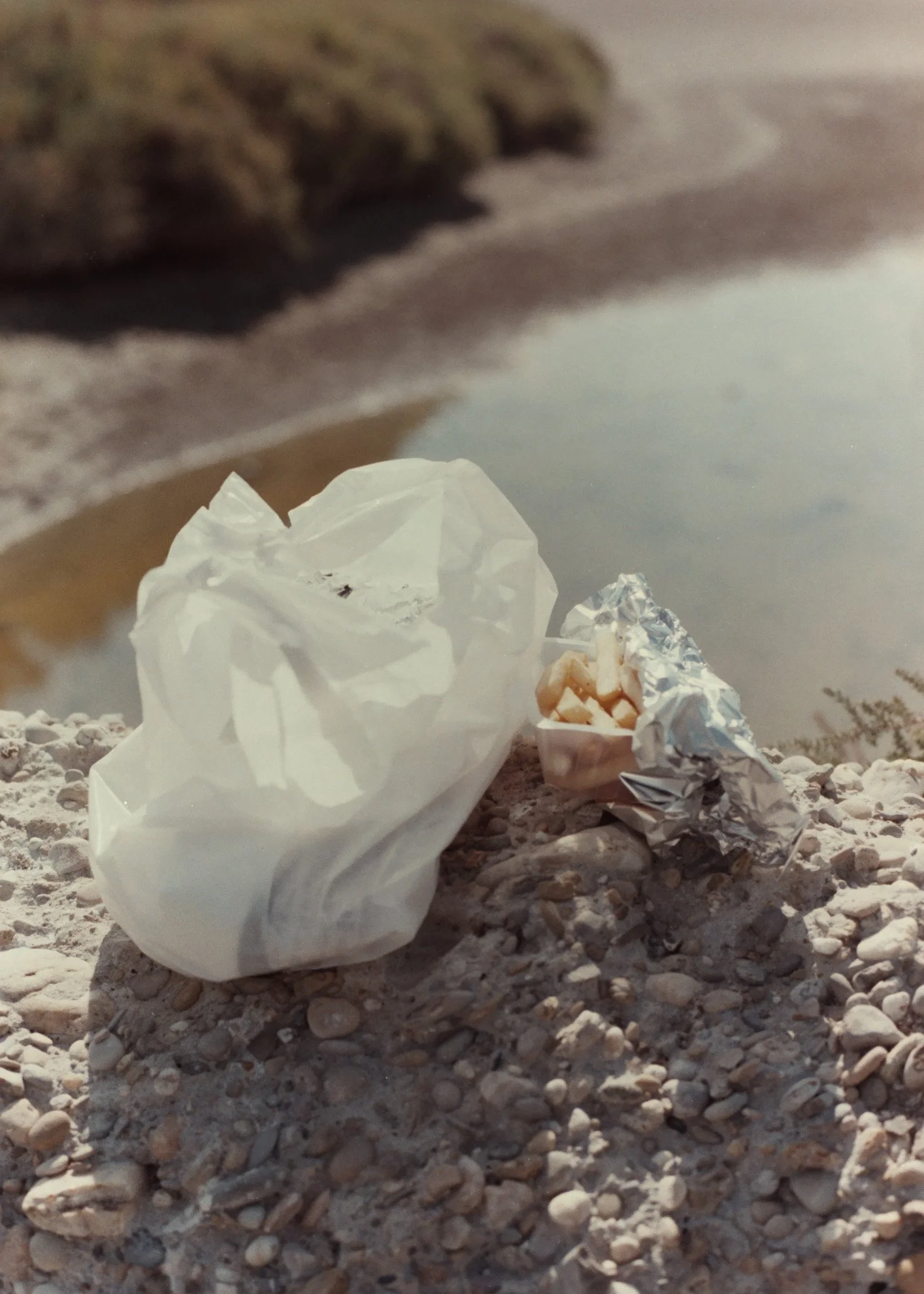 Des déchets en papier et en aluminium abandonnés sur une plage de sable et de petits cailloux.