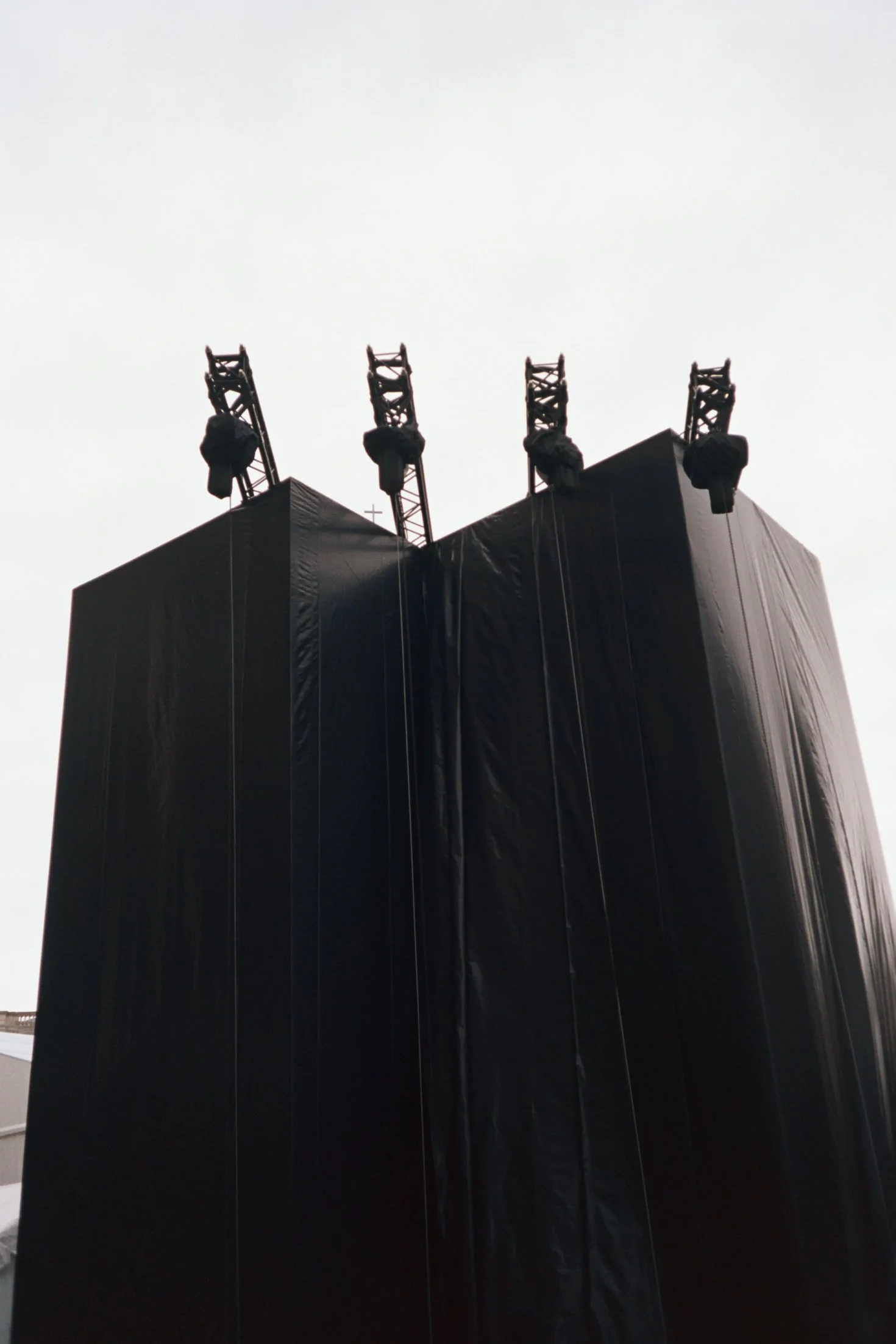 Vue d'une façade sombre d'un bâtiment avec quatre tours de télécommunication en acier noir en haut, contre un ciel gris clair.
