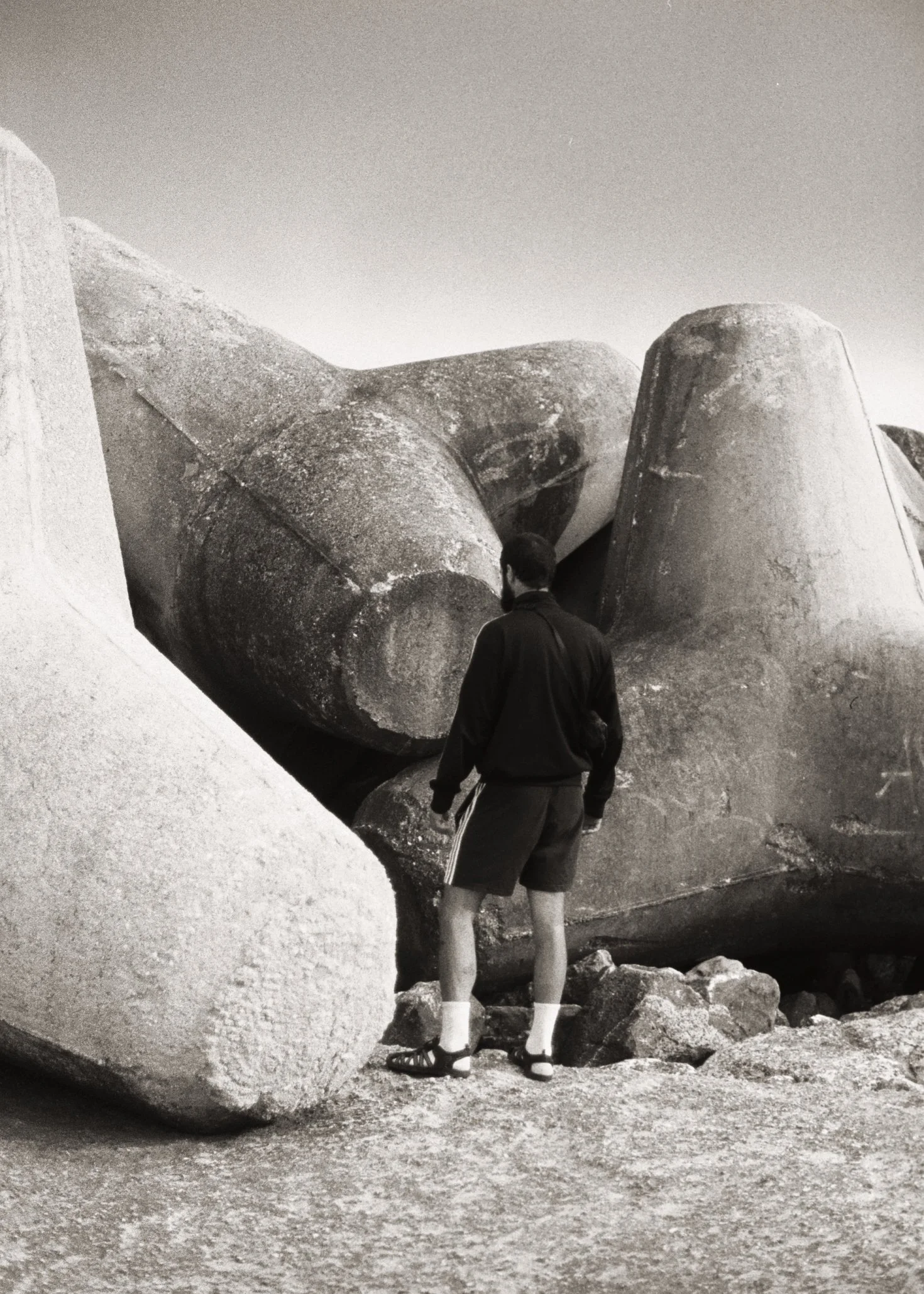 Un homme avec un sac à dos regarde une sculpture géante en pierre sur la plage.