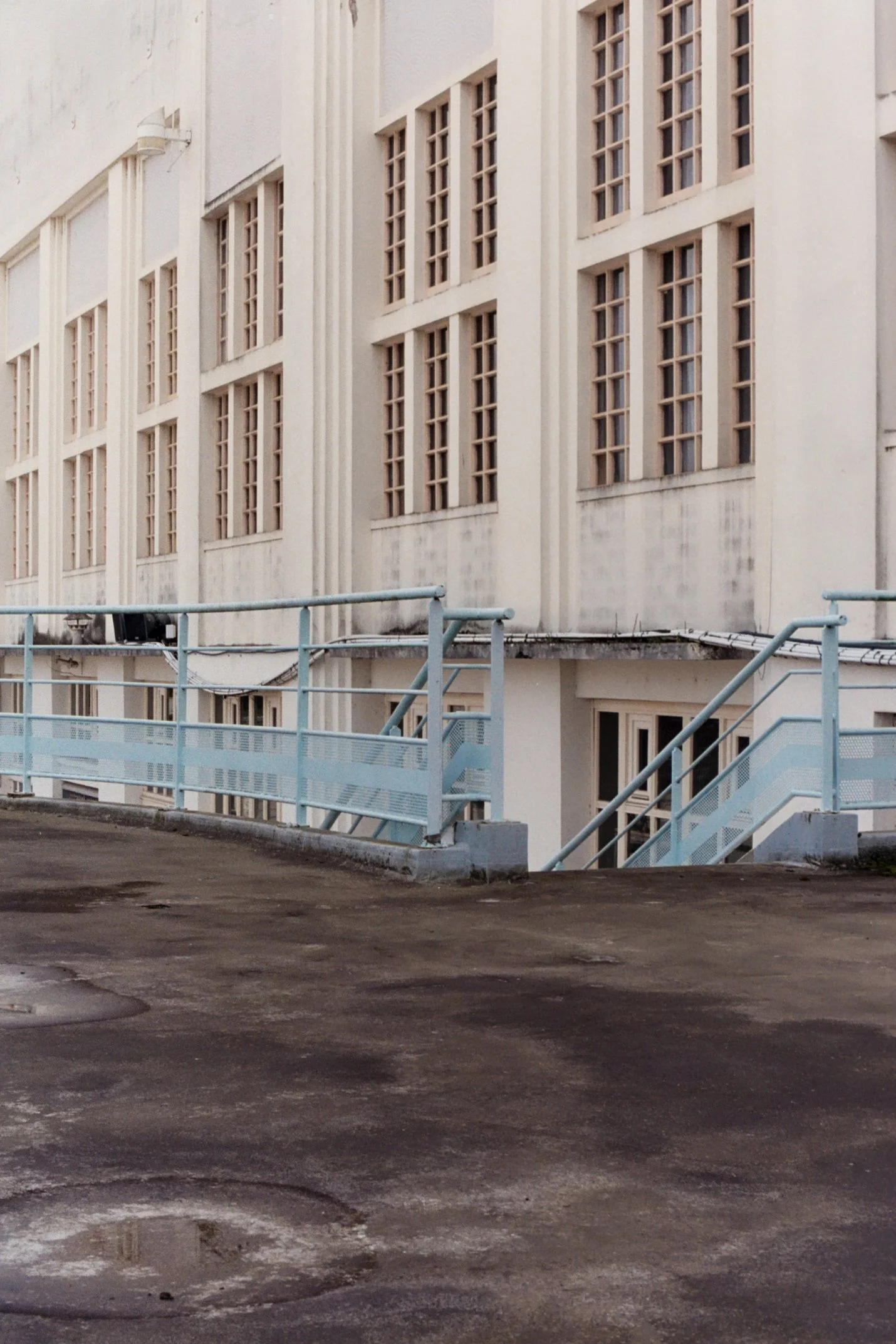Façade d'un bâtiment blanc avec de nombreuses fenêtres à petits carreaux et une rampe d'escalier en métal bleuté en premier plan.