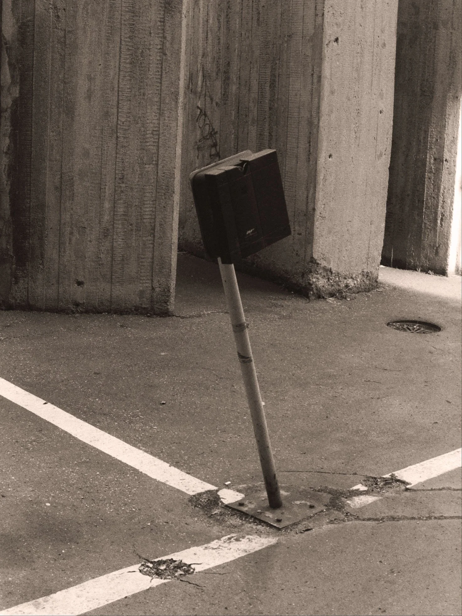 Un poteau abîmé dans un parking près d'un mur en béton, avec une ligne de marquage blanche sur le sol.