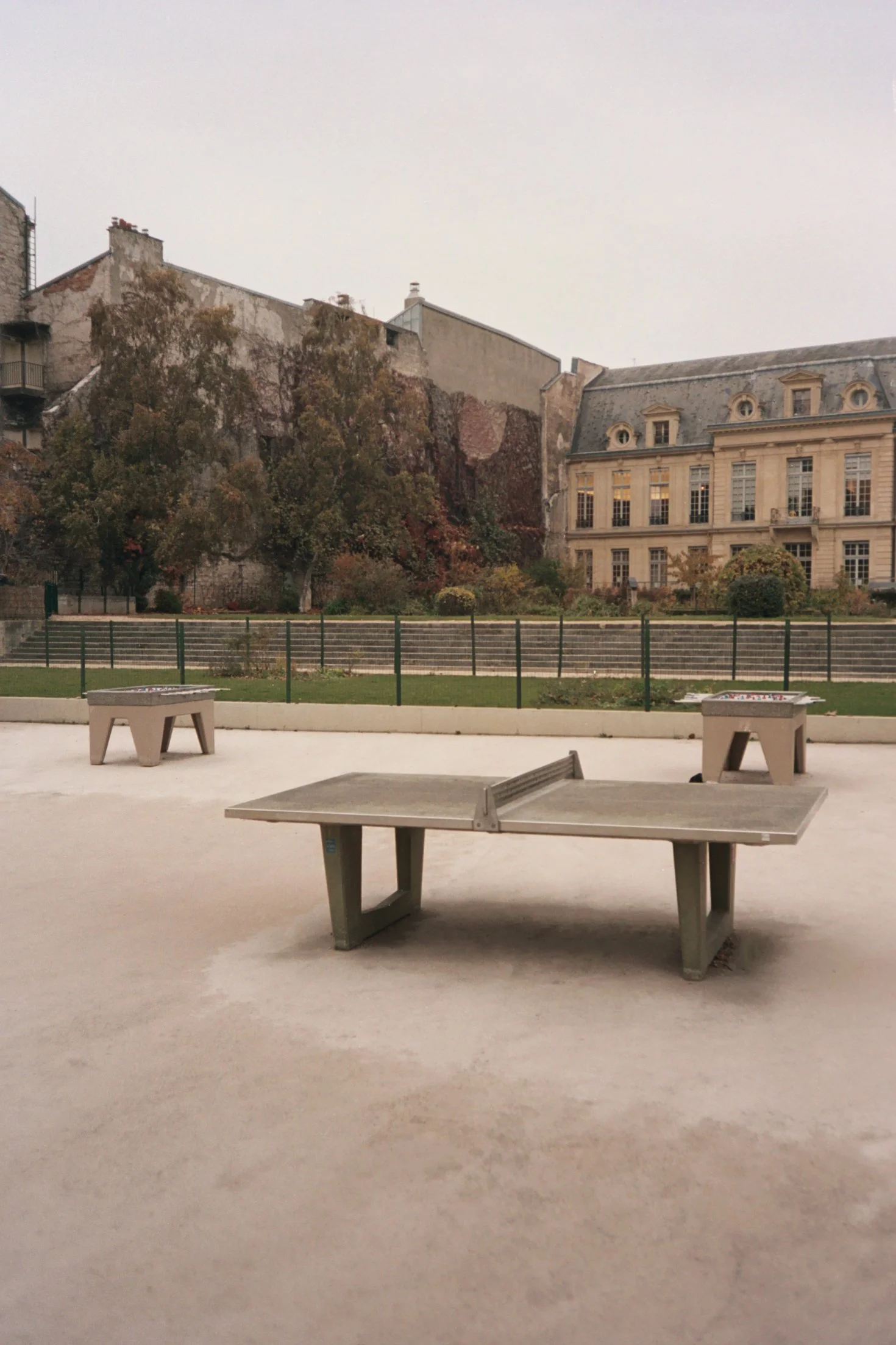 Une cour extérieure avec des tables de ping-pong en béton et un bâtiment historique en arrière-plan, entouré d'arbres.