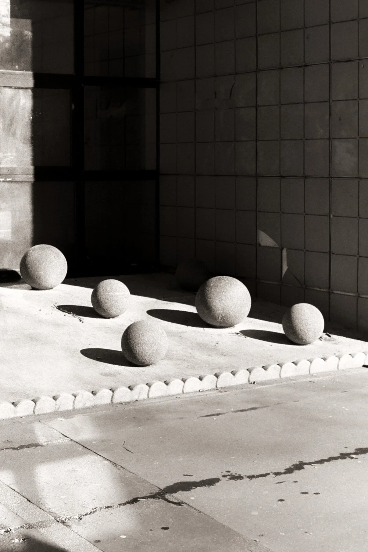 Sculpture urbaine de boules en pierre placées sur le sol, avec des ombres longues, devant un mur en briques, dans un environnement urbain.