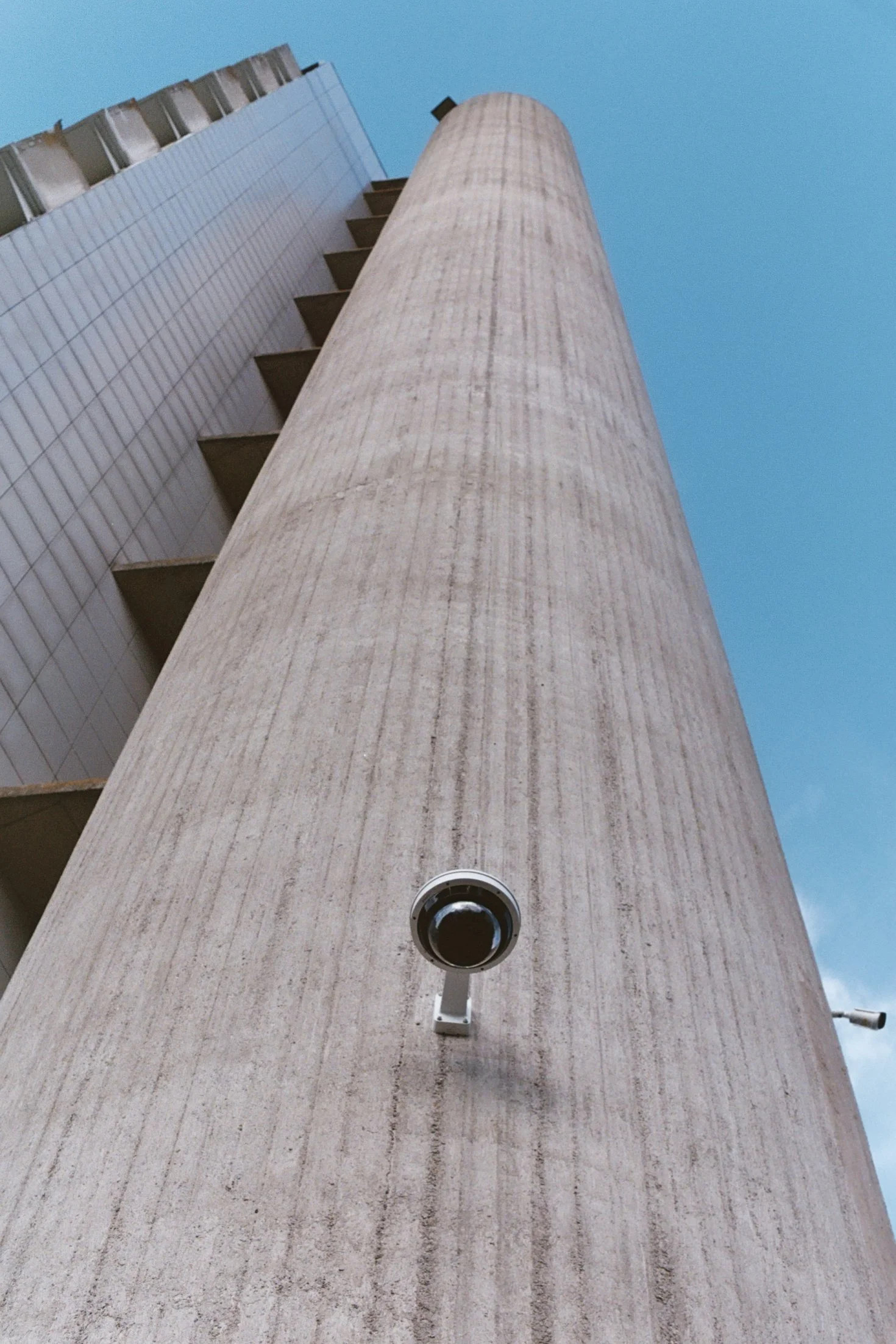 Vue en contre-plongée sur un bâtiment moderne avec une grande colonne en béton et des caméras de surveillance.