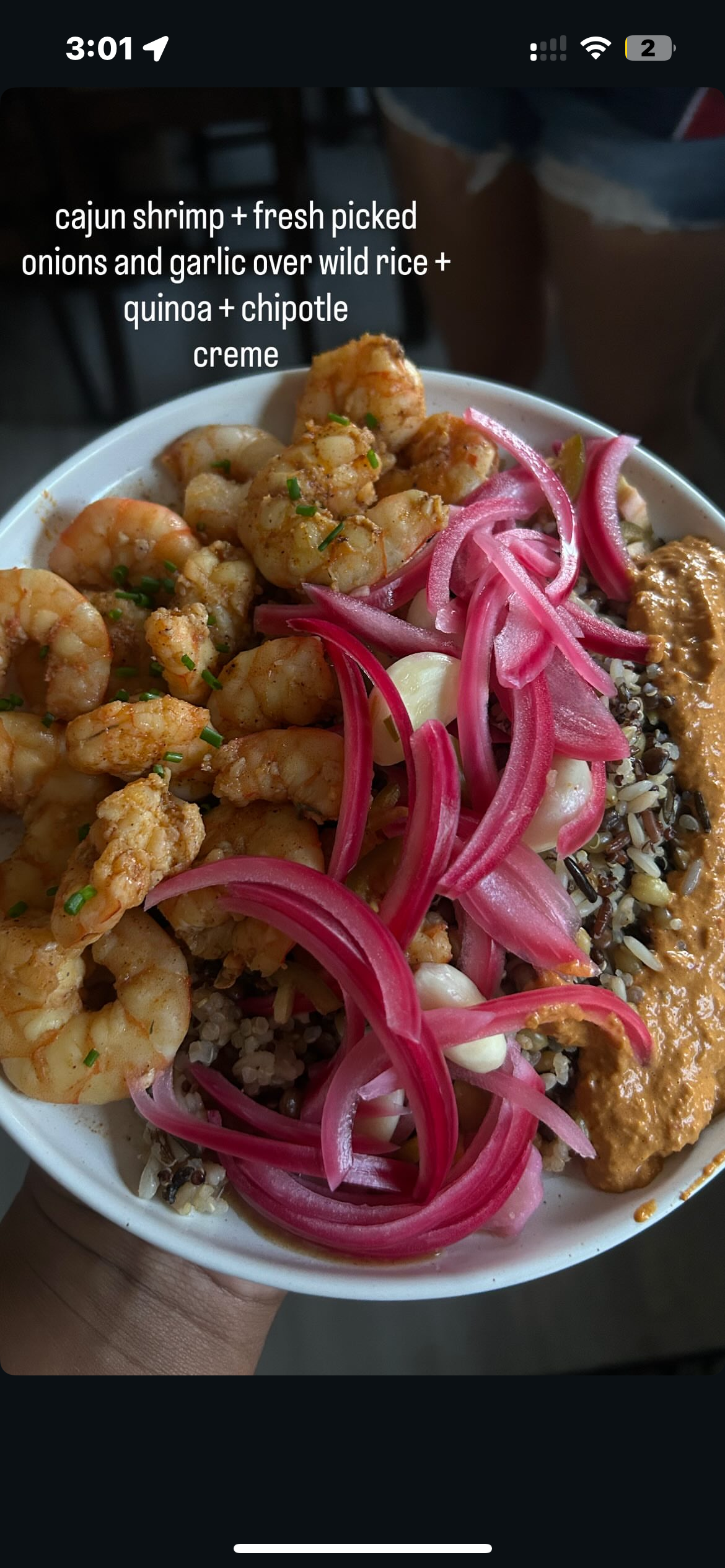 Close-up of a bowl with Cajun shrimp, pickled onions, garlic, wild rice, quinoa, and chipotle creme.