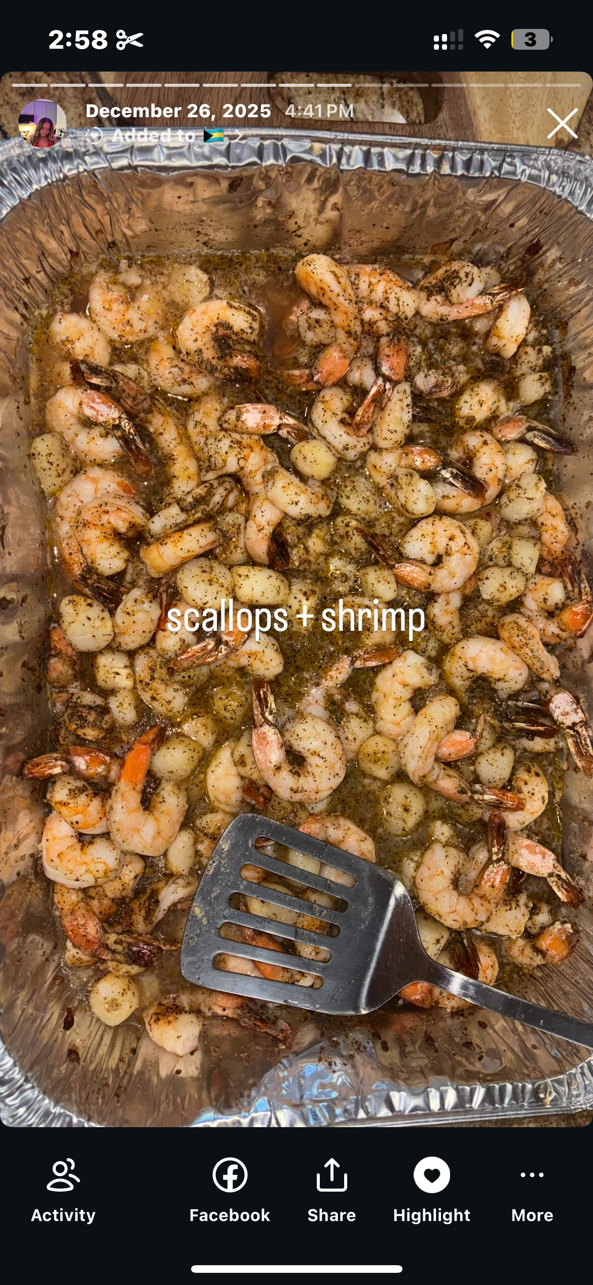Cooked shrimp seasoned with herbs and spices, labeled as scallops + shrimp in a foil tray with a spatula.