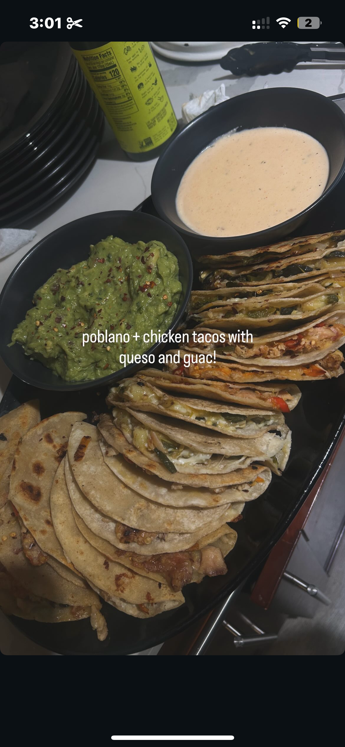 A tray of chicken and veggie tacos with guacamole, served with queso dip and a bowl of creamy soup, featuring a can of Mexican soda and some plates in the background.