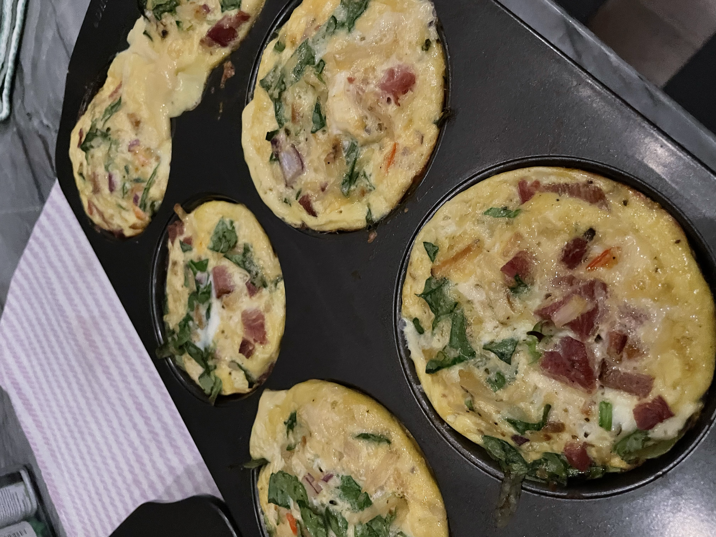 Mini frittatas with eggs, chopped vegetables, and pieces of ham in a muffin tin.