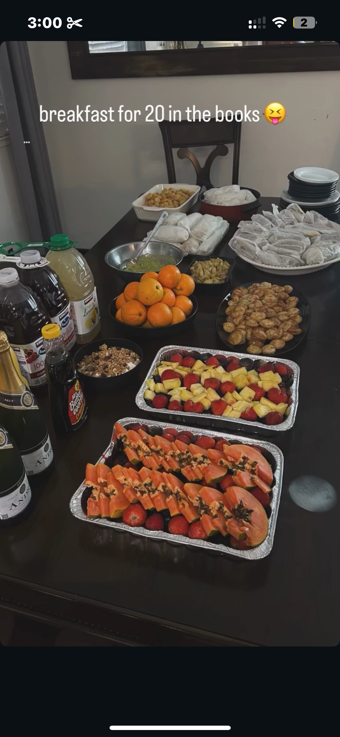 Table filled with various breakfast foods including sliced fruit, oranges, grapes, pastries, juice bottles, and condiments.