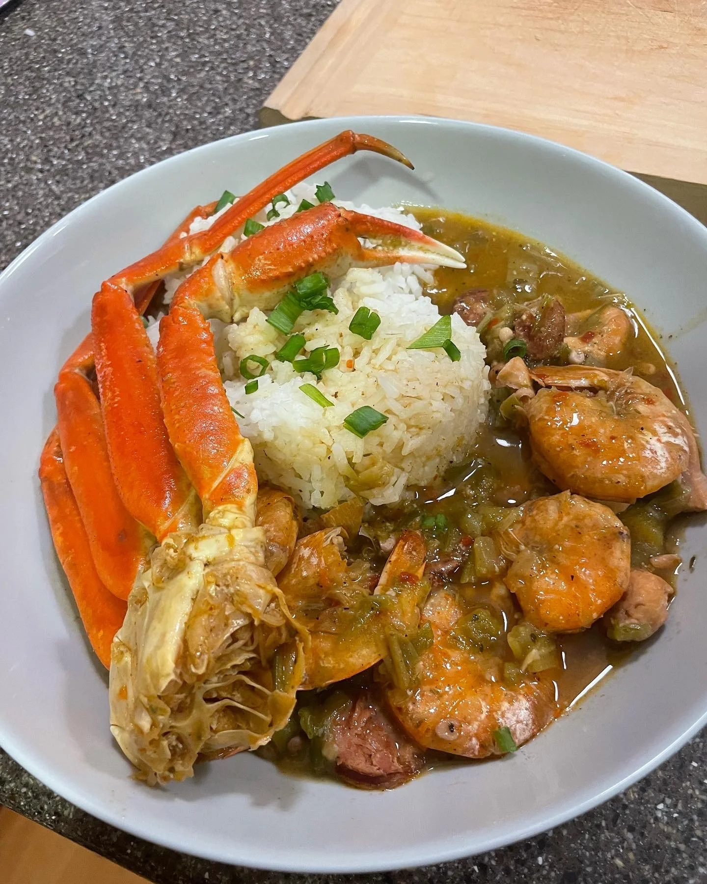 Seafood dish with rice, crab legs, shrimp, and sausage in a savory sauce garnished with chopped green onions.