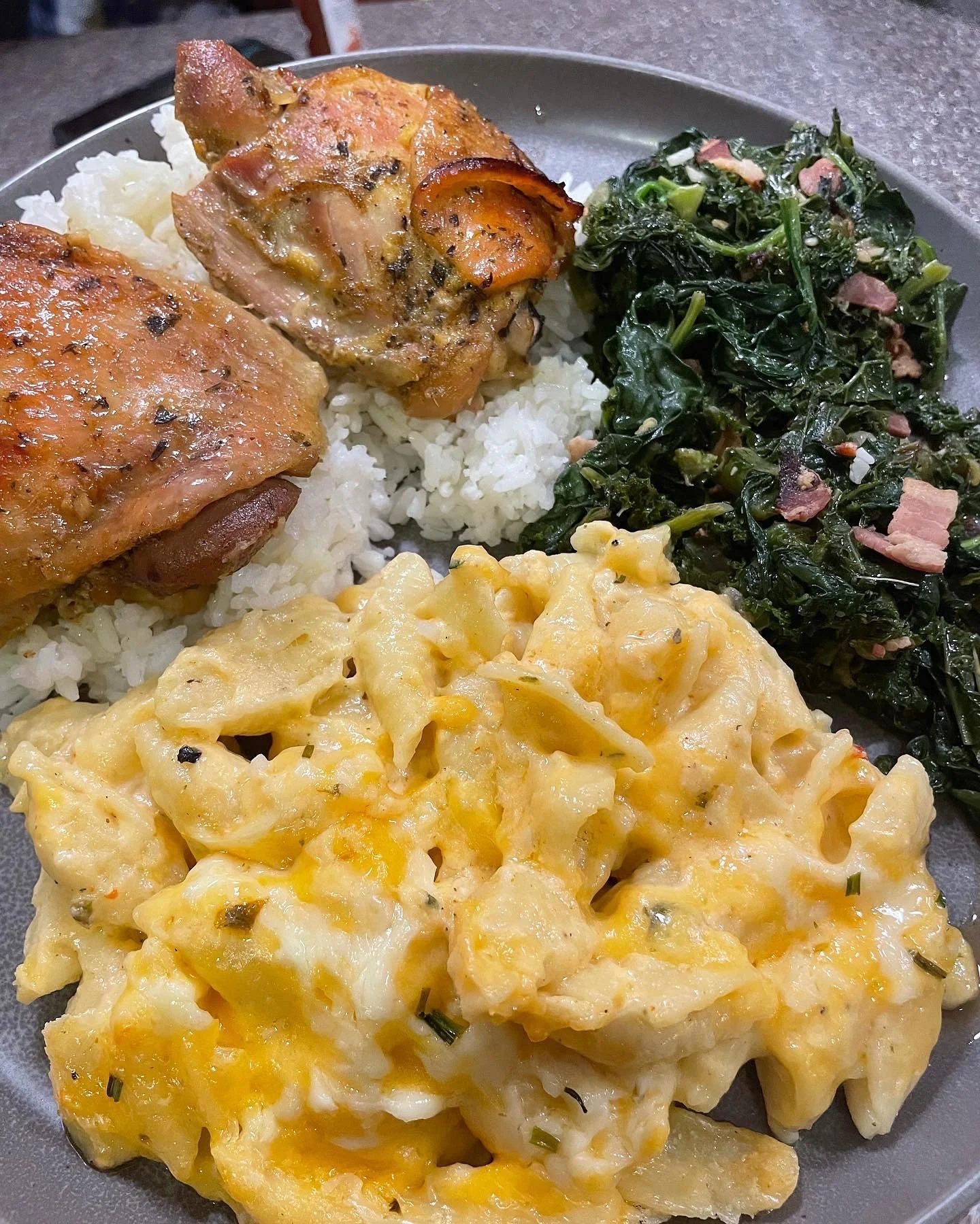 A plate of food with baked chicken, macaroni and cheese, sautéed kale with ham, and white rice.