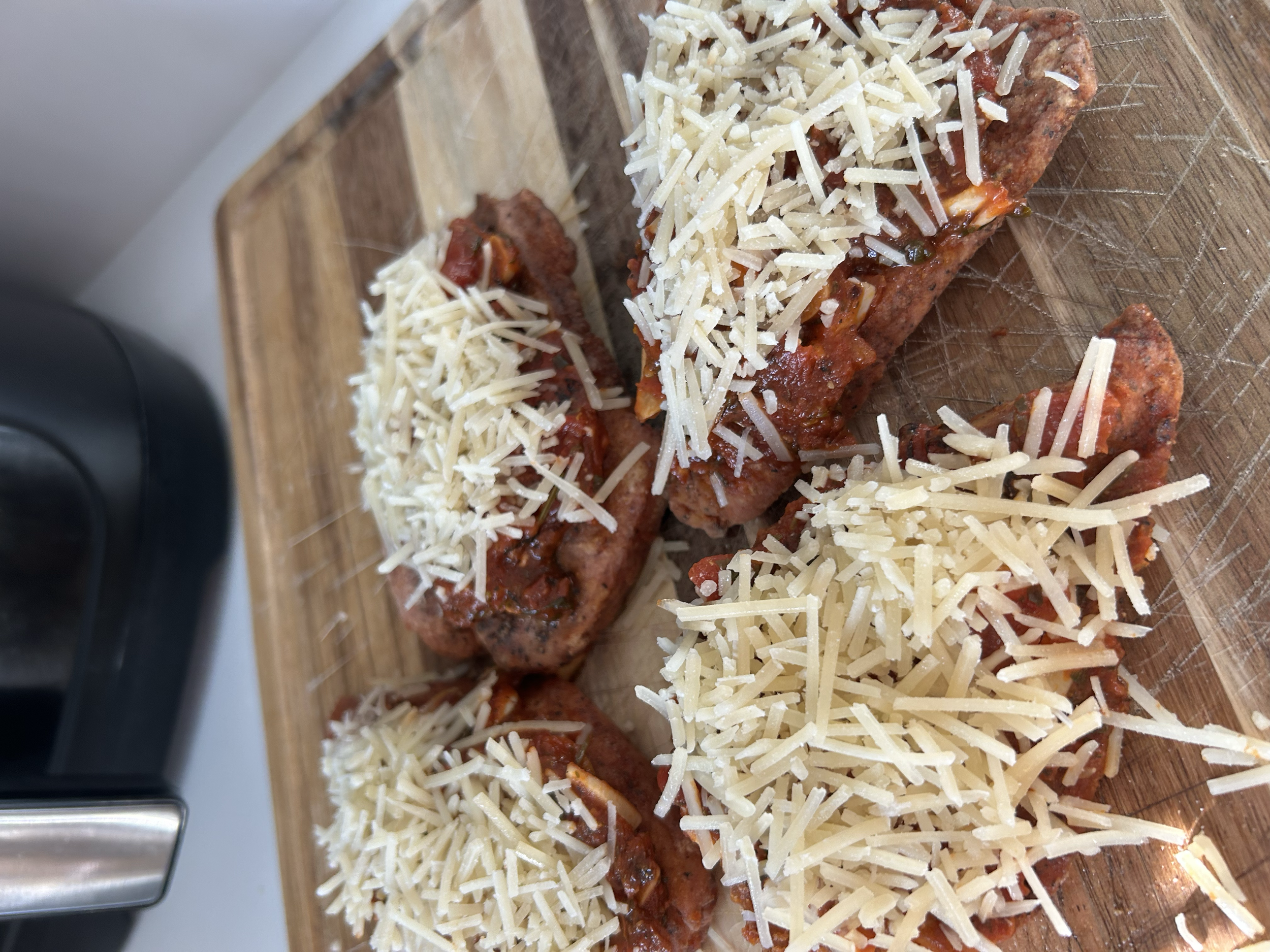 Three pieces of lasagna with cheese on top placed on a wooden cutting board.