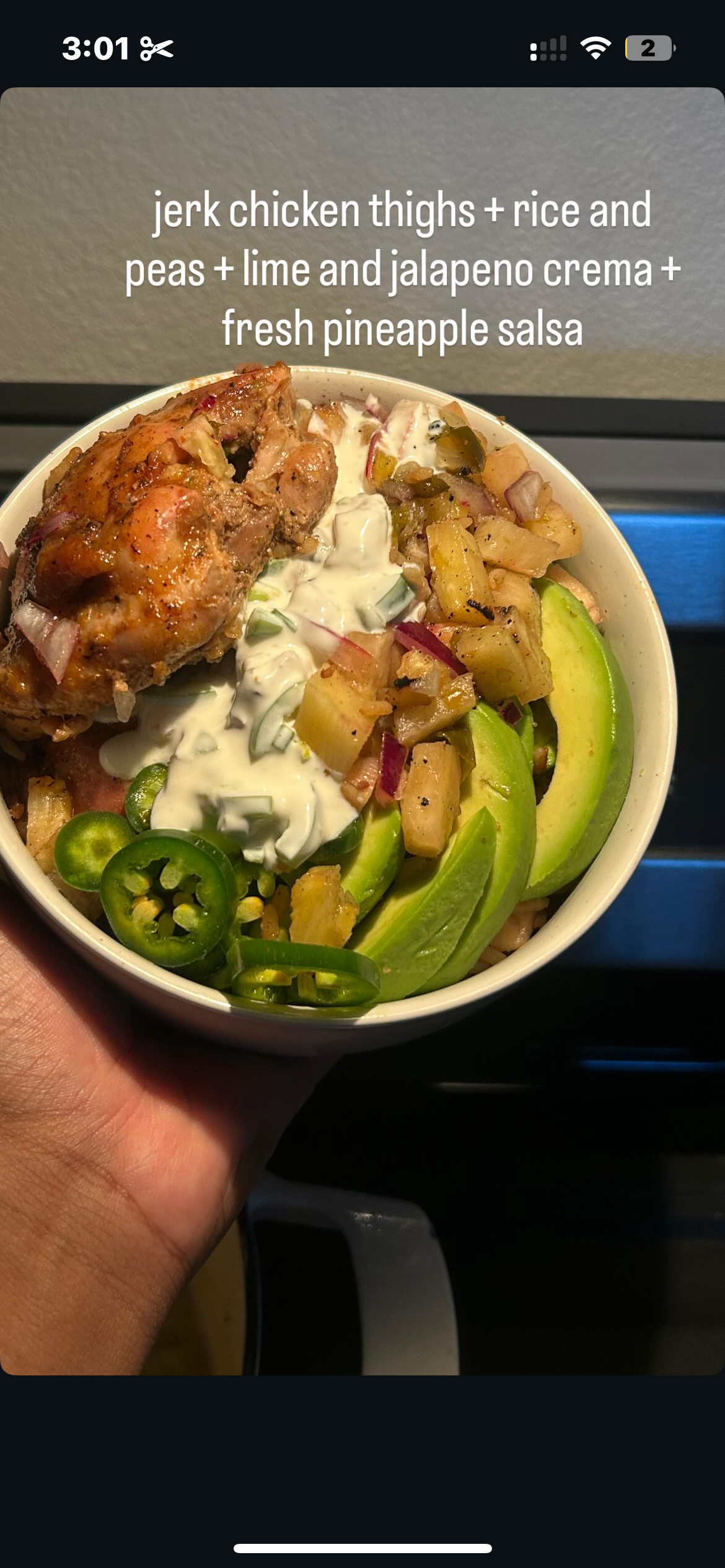 A bowl of food with jerk chicken thighs, rice and peas, lime and jalapeno crema, and fresh pineapple salsa.