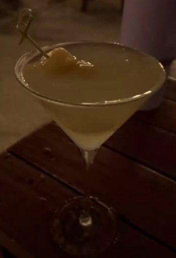 A yellow cocktail garnished with a lemon slice in a martini glass on a wooden table.