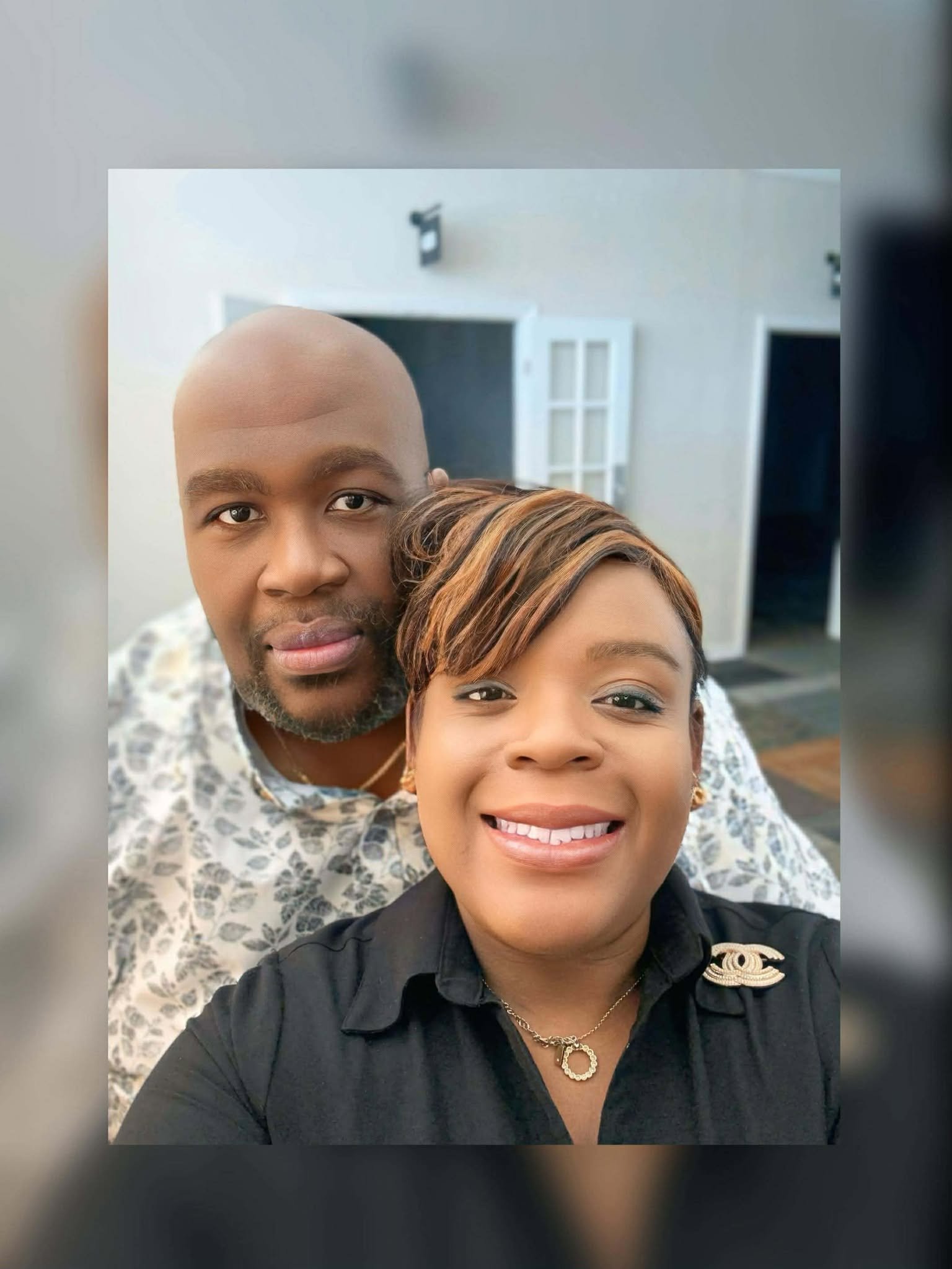 A smiling woman with short hair and a woman with a bald head, both posing for a selfie indoors.