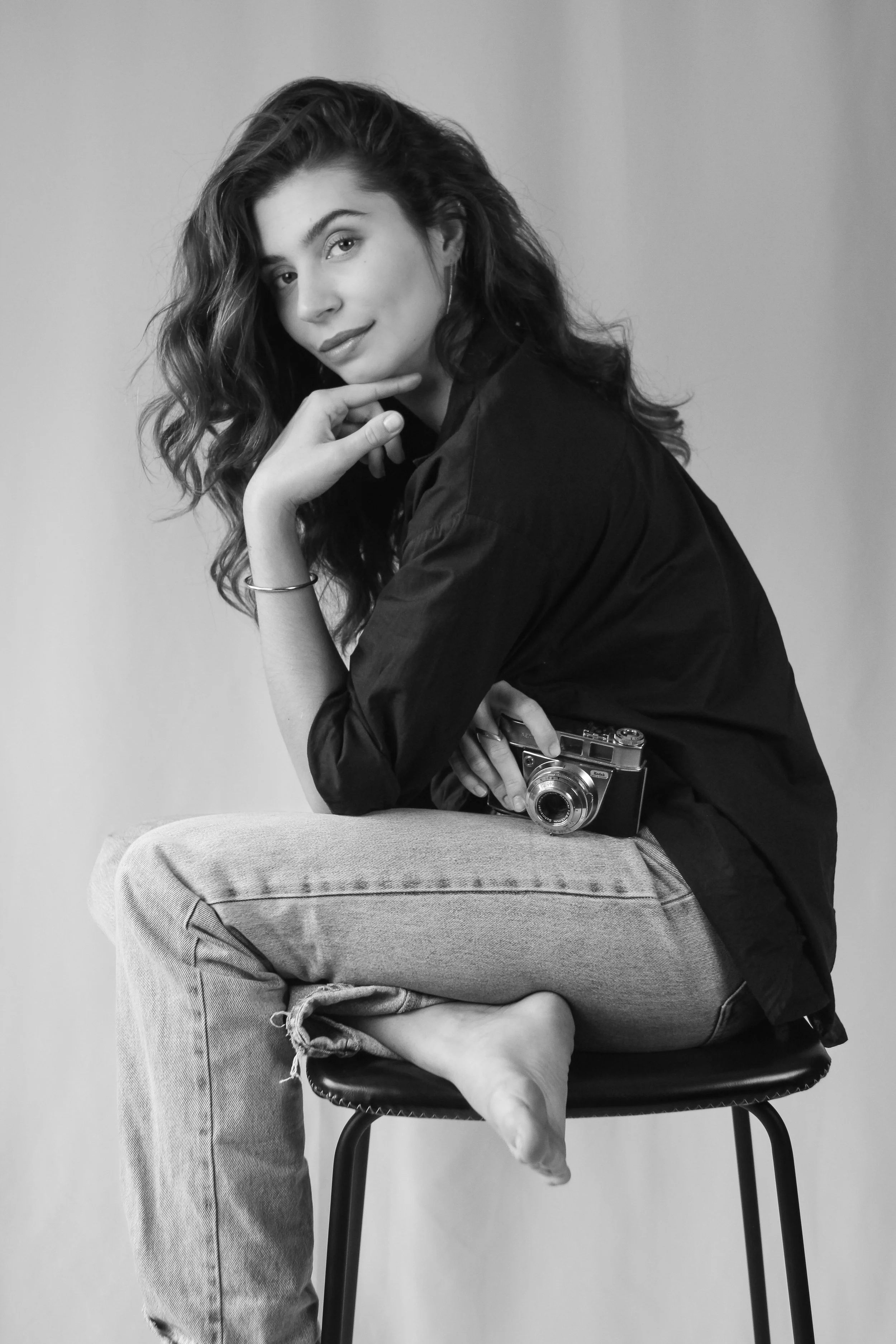 Jeune femme assise sur une chaise, tenant un appareil photo, en style noir et blanc.