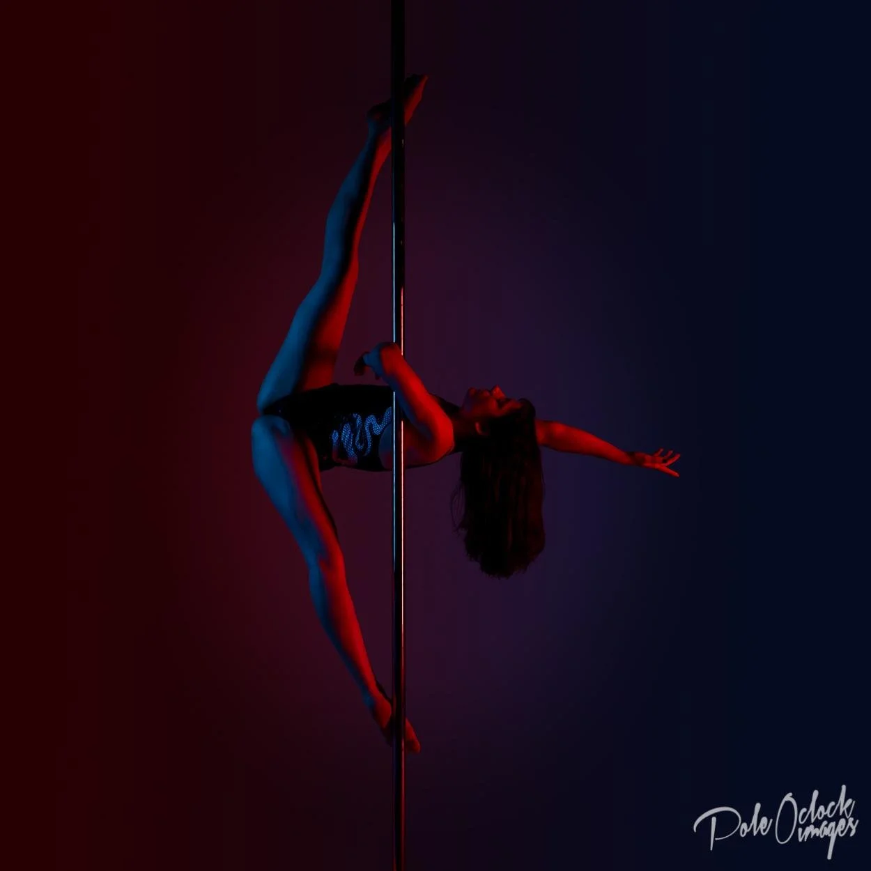 A female pole dancer performing on a pole, illuminated with red and blue lighting, with one arm extended and her body in an arched pose.