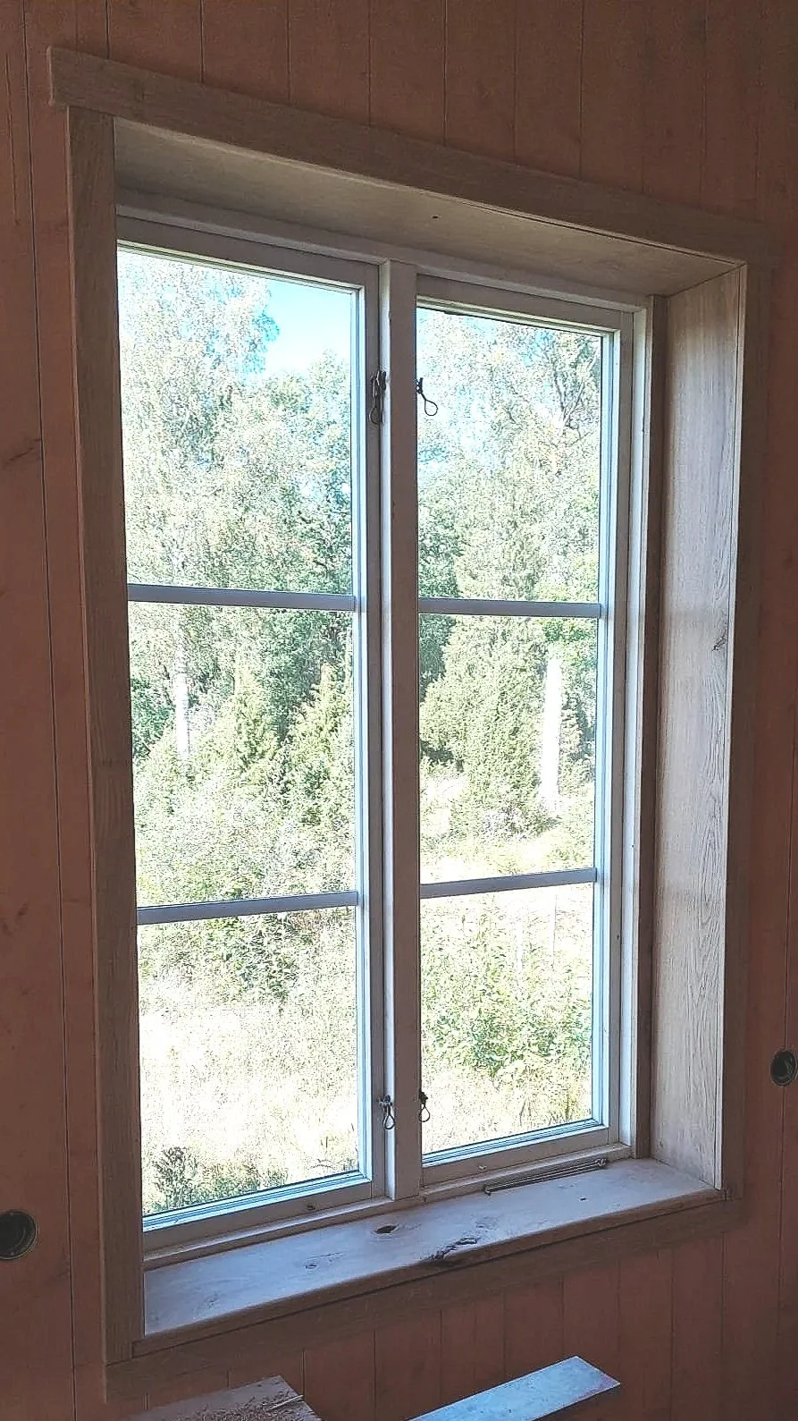 Binnenkant van een kamer met een nieuw geschilderde houten raambouw en een open raam met uitzicht op groene bomen en een zonnige dag.