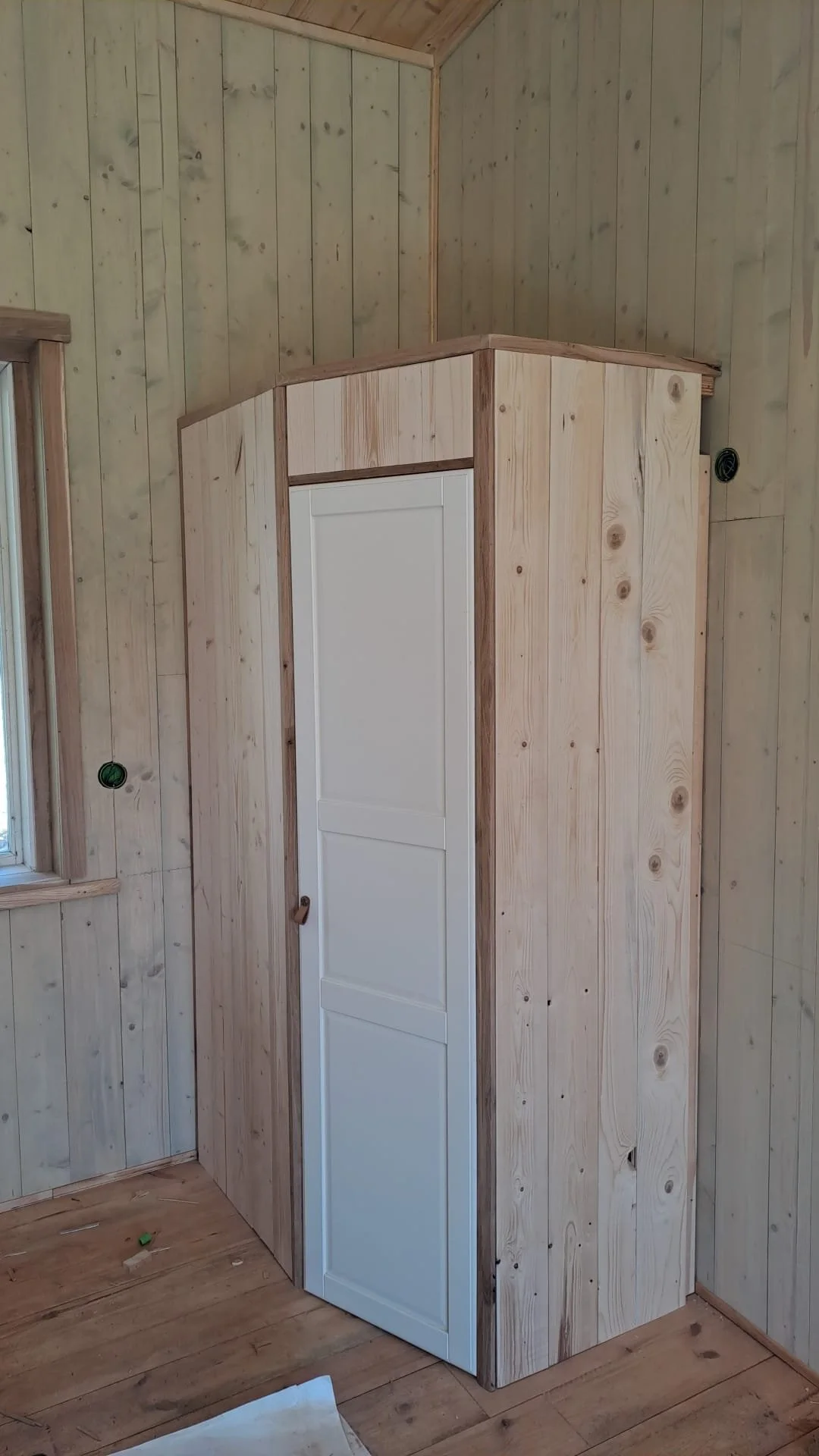 Een houten kast met een witte deur, geplaatst in een houten kamer onder een schuine houten plafond.