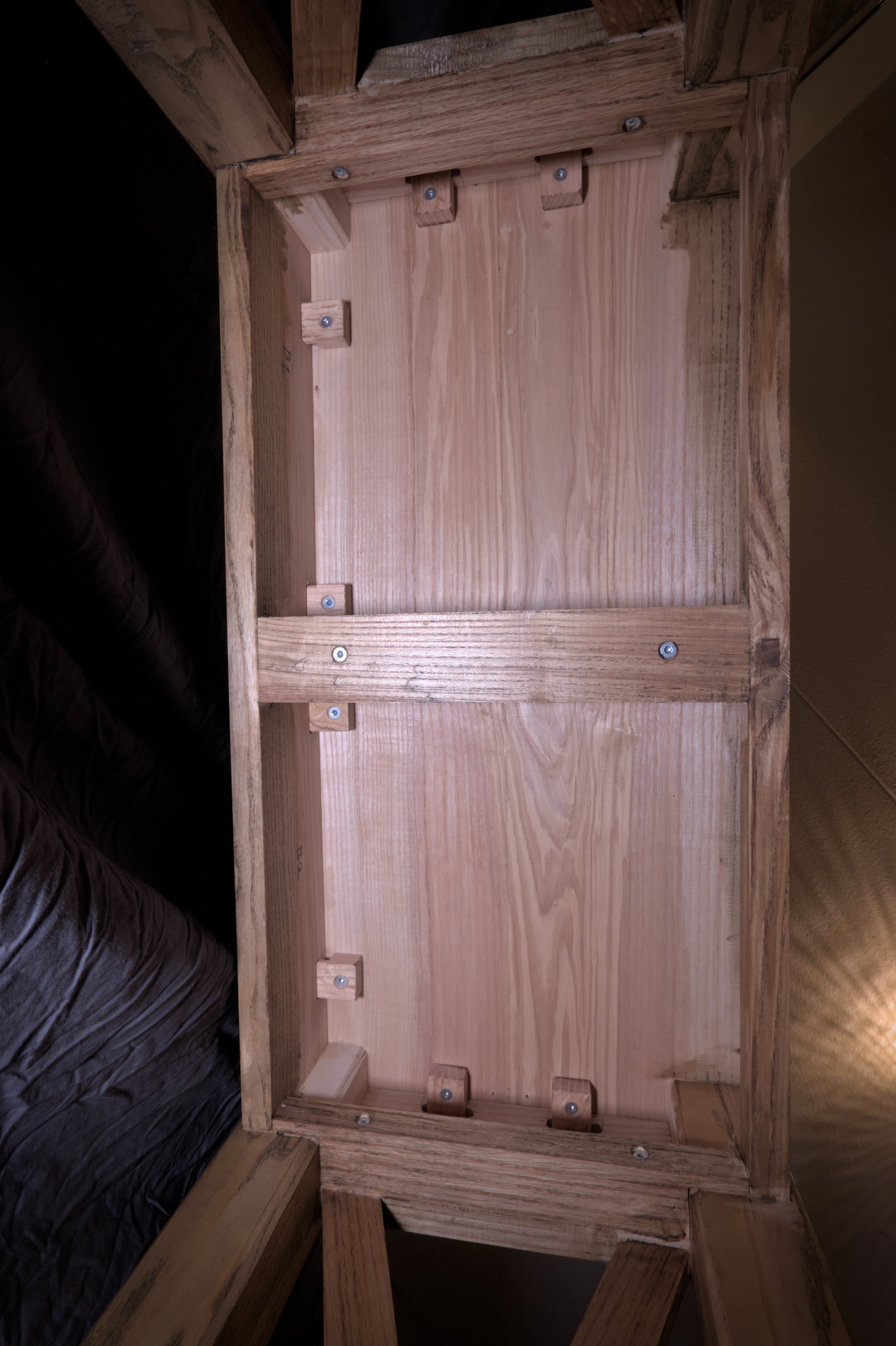 De onderkant van een houten meubelstuk of drager met zichtbaar bevestigingsmateriaal en houten planken.