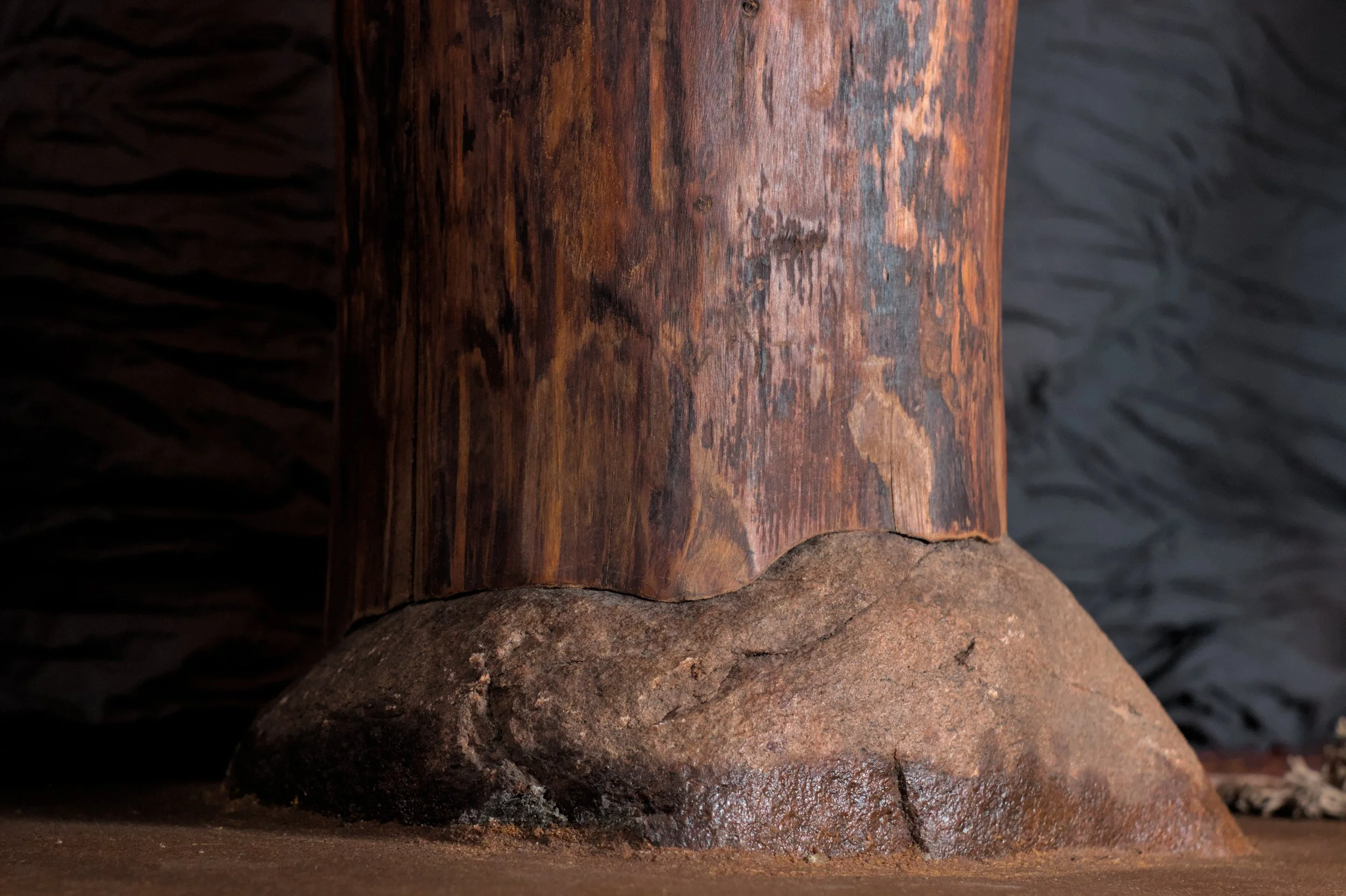 Close-up van een houten pilaar die op een rots staat, met een donkere achtergrond