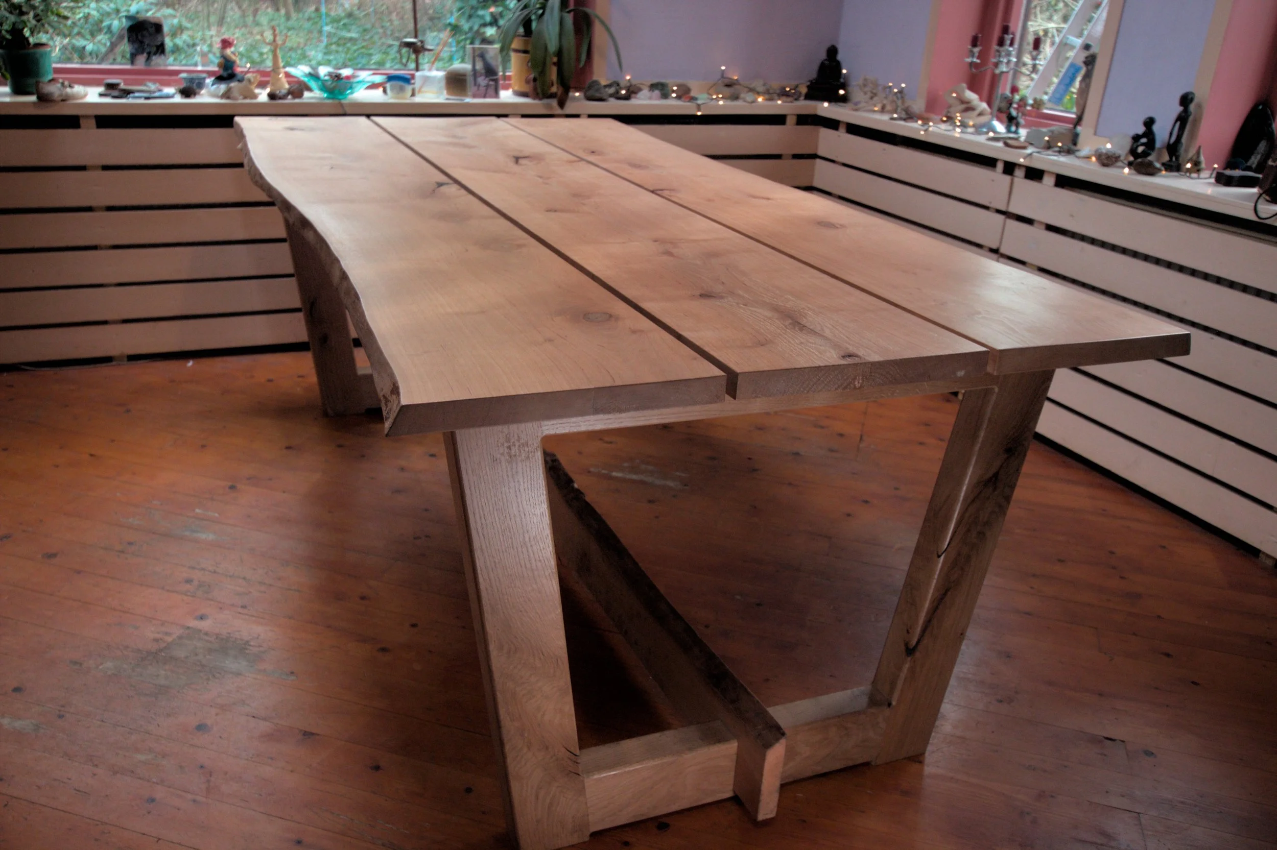 Een massief houten eettafel in een interieur met houten vloer, versierd met kleine decoraties en planten op de vensterbank.