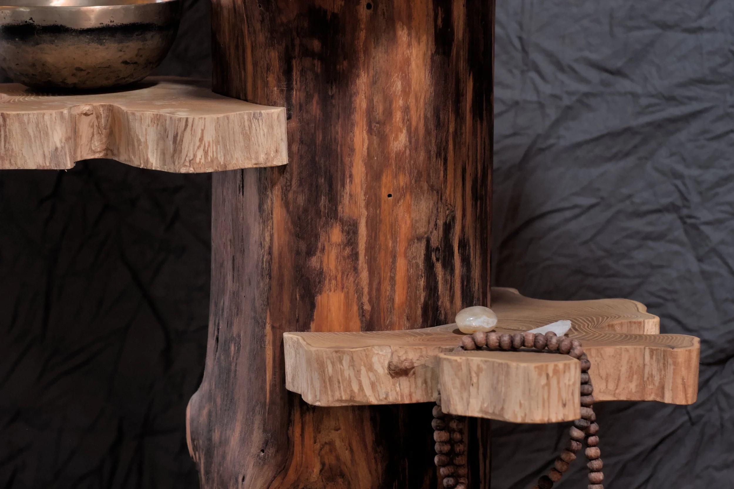 Close-up van een houten sculptuur met planken en een kralenketting en een steen erop.